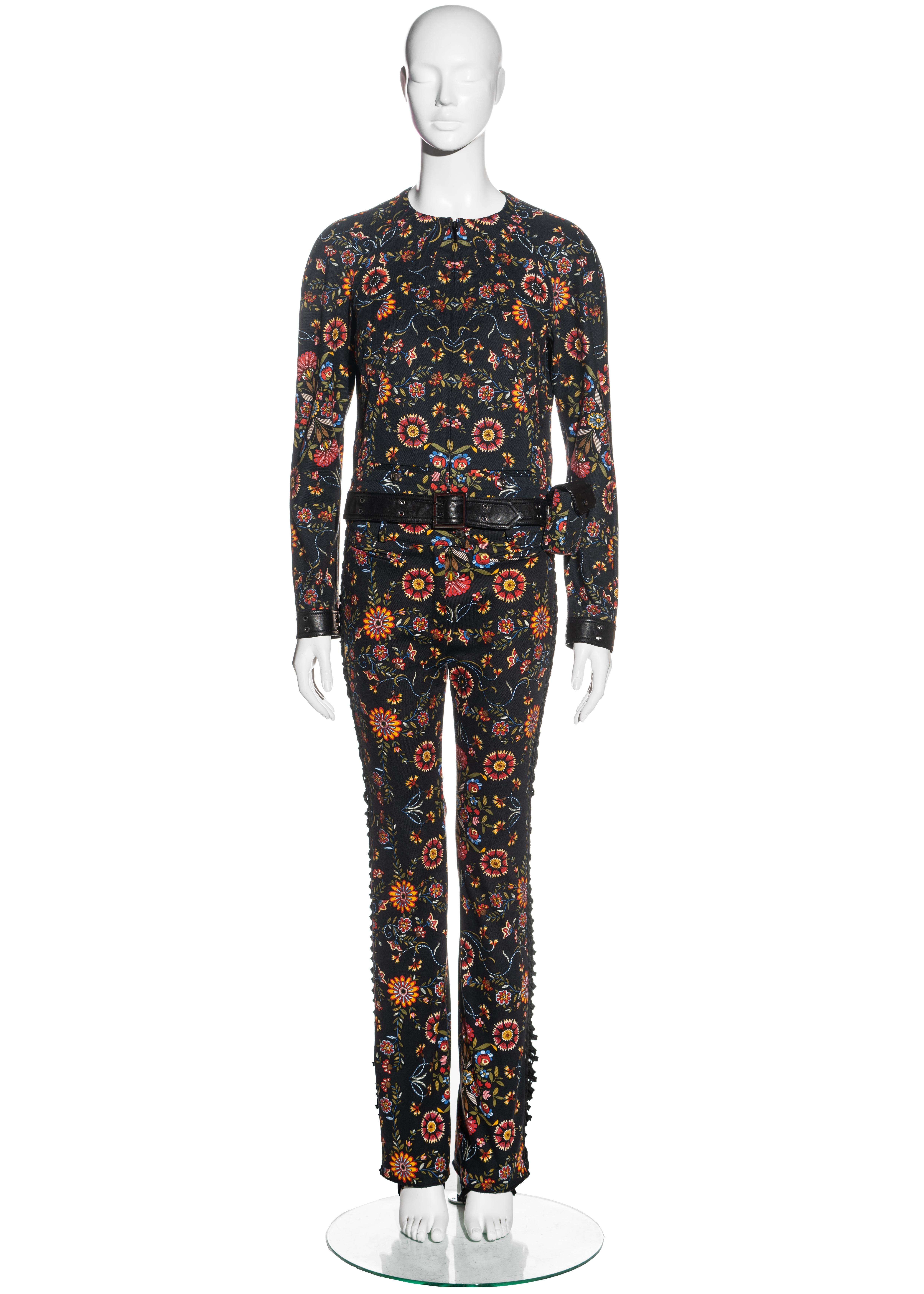 ▪ Christian Dior floral cotton and leather pant suit
▪ Designed by John Galliano
▪ 98% Cotton 2% Elastane / 100% Leather 
▪ Round neck zip-up jacket 
▪ Attached leather belt with metal buckle and grommets 
▪ Detachable bag on the hip 
▪ Flared pants