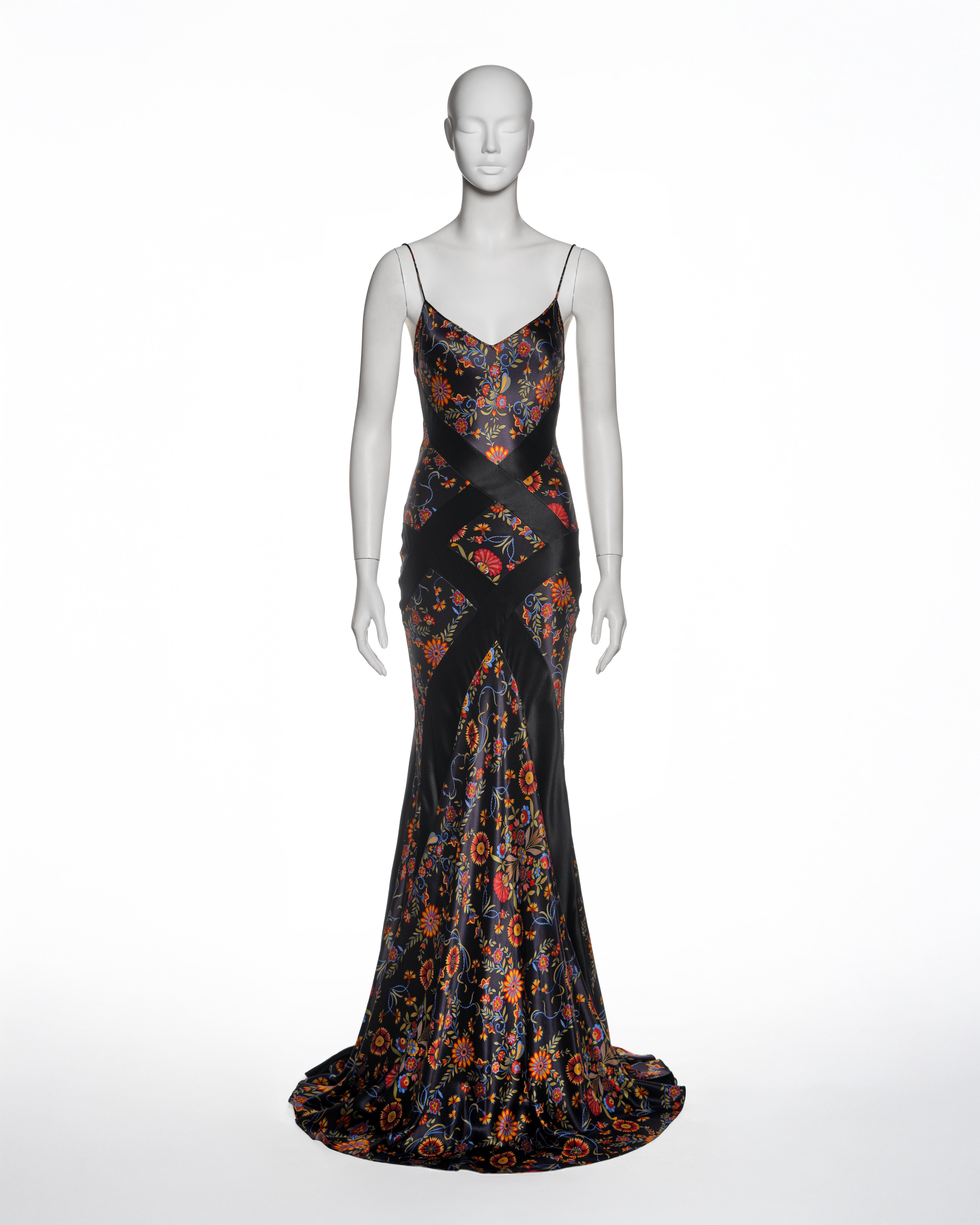 Dieses Kleid von Christian Dior by John Galliano aus der Herbst-Winter-Kollektion 2002 ist ein bodenlanges, figurbetontes Slip-Kleid, das aus schwarzen Satinbahnen besteht, die sich mit floral bedrucktem Satin in leuchtenden Rot-, Orange-, Blau-,