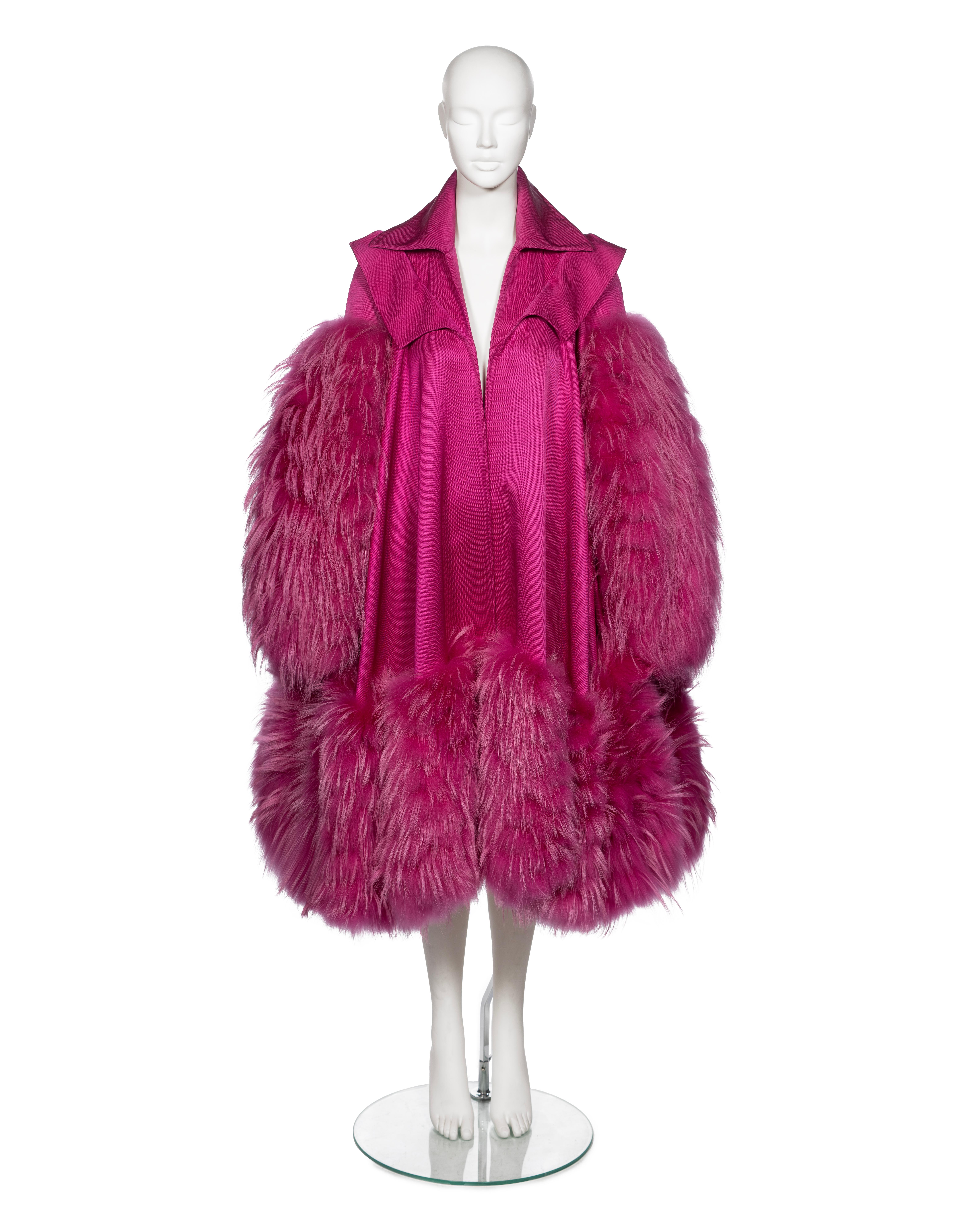 A museum-grade Christian Dior evening coat, crafted from a cotton and silk blend in a rich fuchsia hue. The coat features dramatic, oversized raccoon fur trim on the sleeves and hem, an A-line silhouette, fully lined in silk and a double-layered