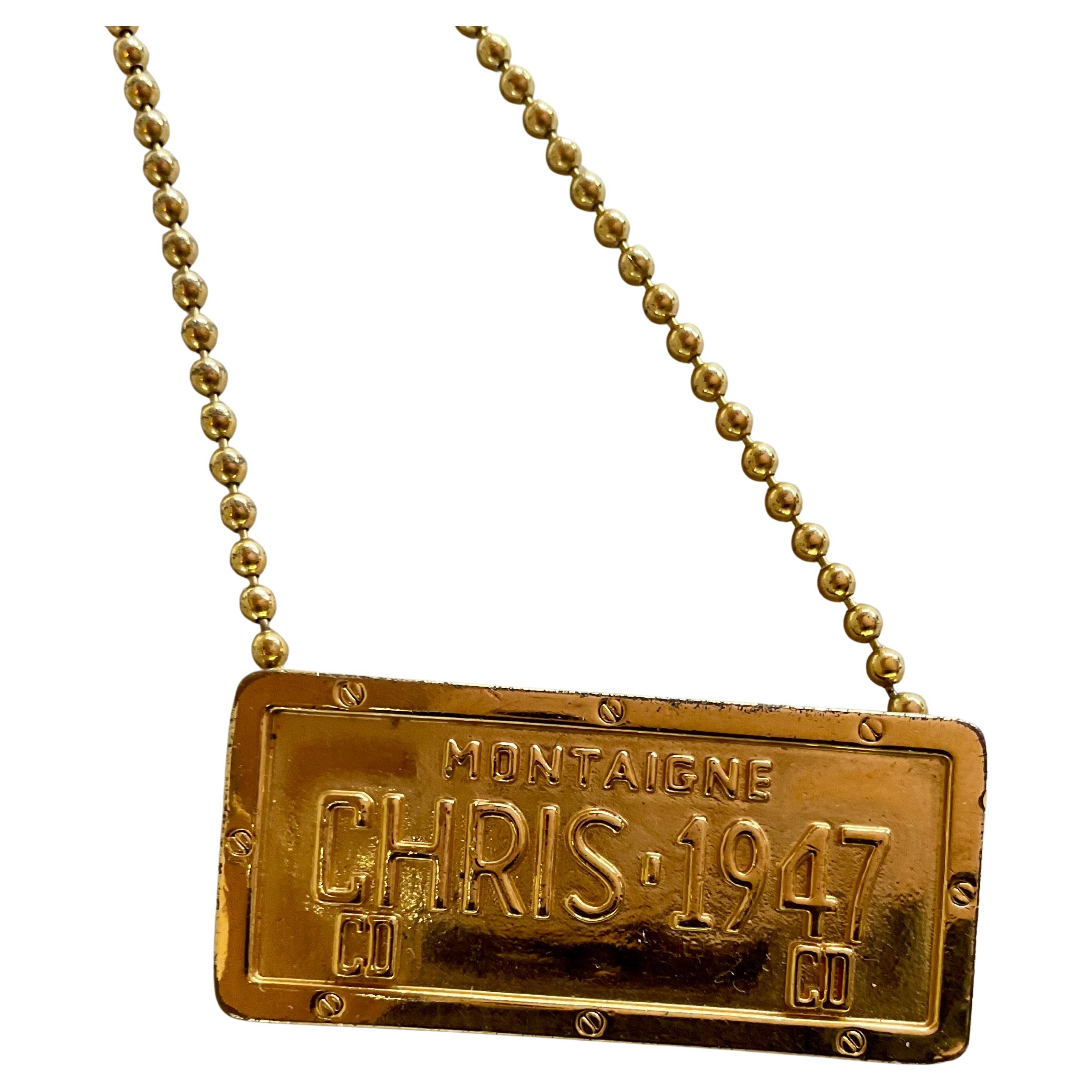 Un collier Christian Dior rare et saisissant de l'époque emblématique de John Galillac, présentant une plaque d'immatriculation Cadillac en métal doré poli et un pendentif assorti, suspendus à une chaîne raffinée. Le collier se termine par un