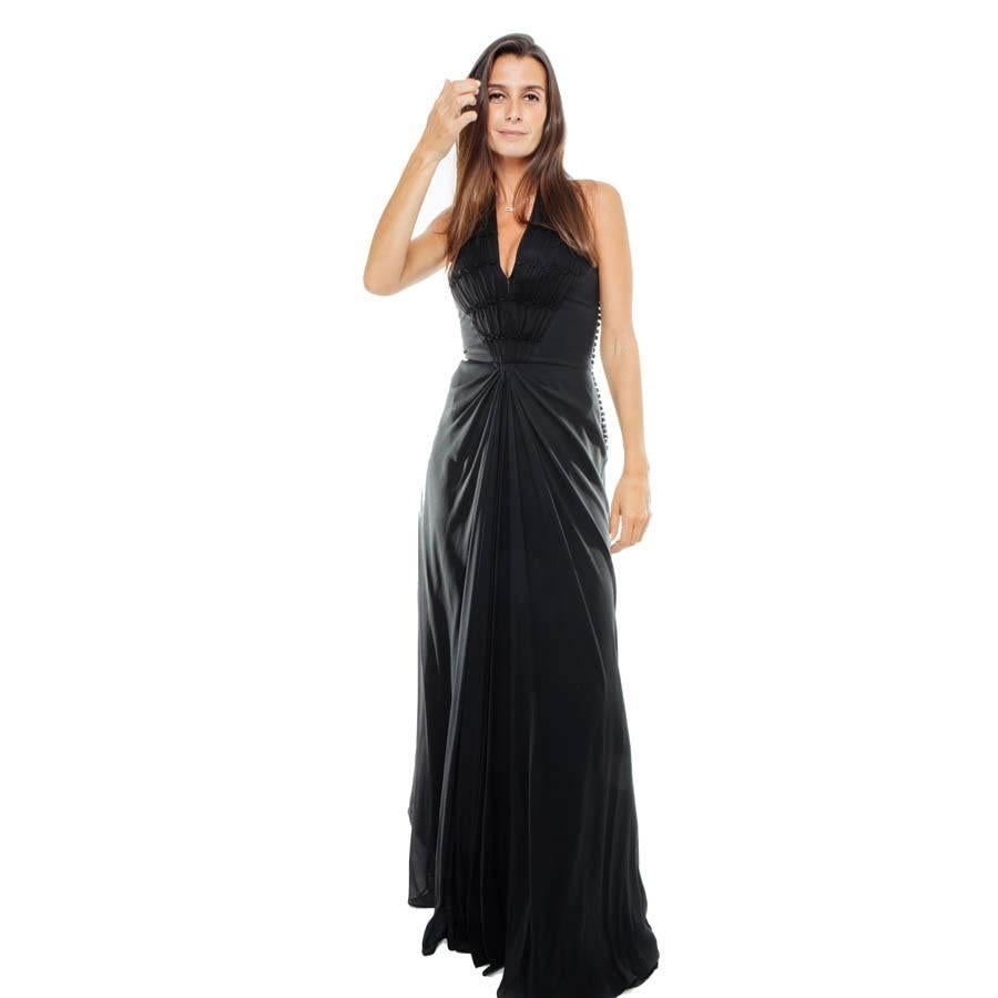 Vestido largo Christian Dior by John Galliano de seda negra. Sin mangas y sin espalda, sujeto en el cuello mediante corchetes invisibles. Se cierra con una serie de pequeños botones en el lado izquierdo del vestido. Hay humos en el pecho y una