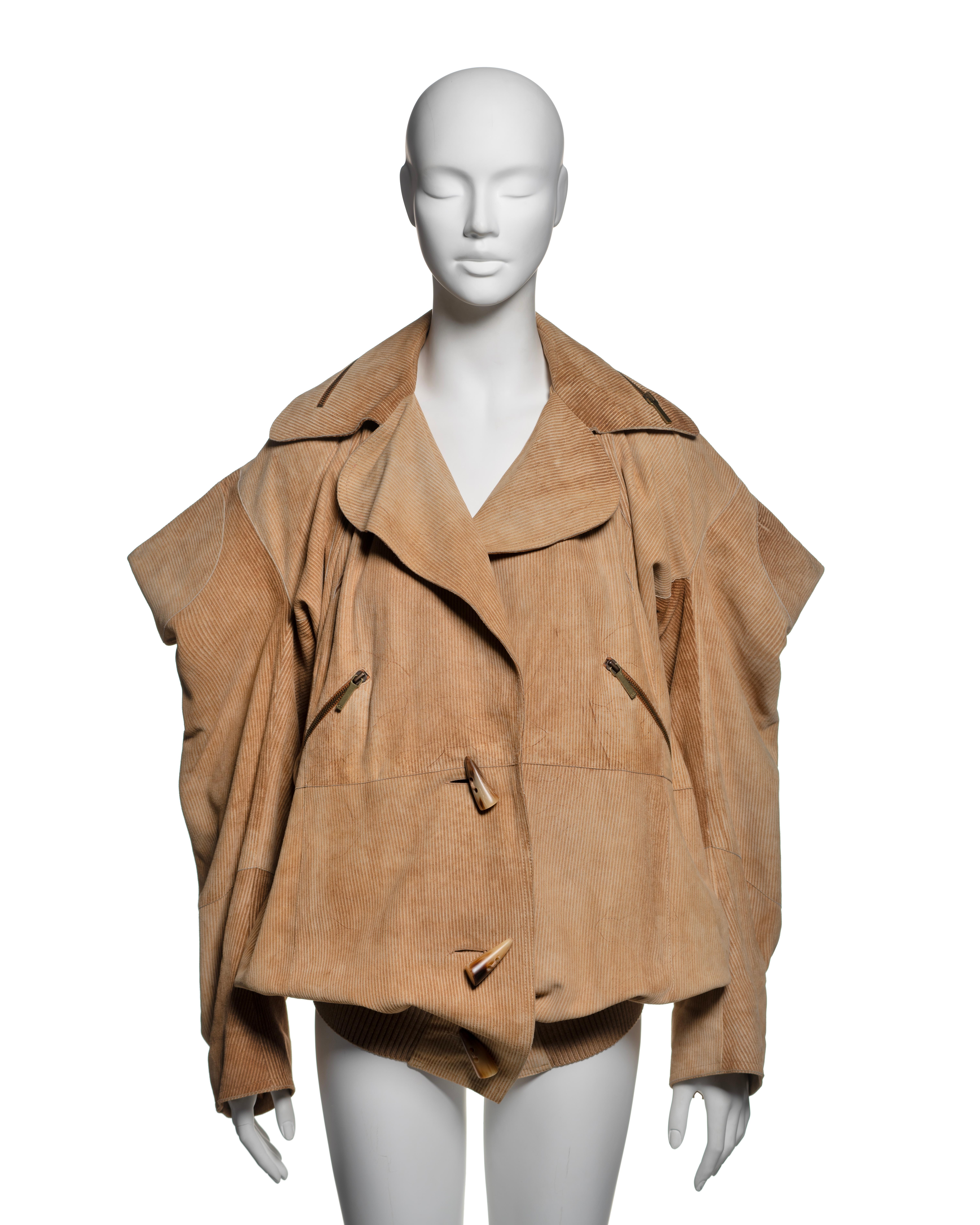 This Christian Dior jacket from the Fall-Winter 2002 collection is constructed from tan goat leather with a fine corduroy texture. It features an oversized, voluminous silhouette with a wide notched collar and dramatic draped sleeves, contributing