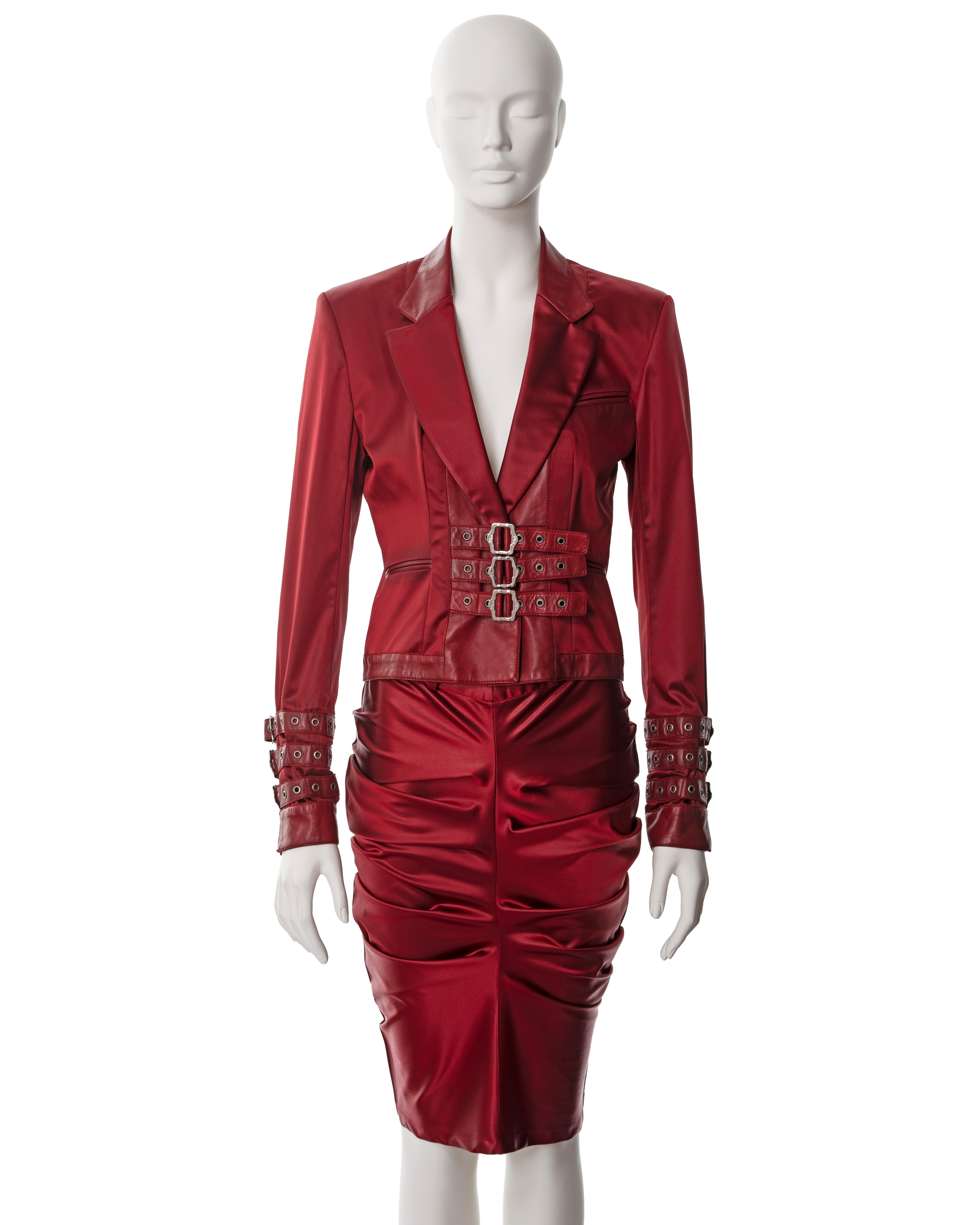 ▪ Christian Dior red satin skirt suit 
▪ Designed by John Galliano
▪ Sold by One of a Kind Archive
▪ Fall-Winter 2003
▪ Constructed from red satin and leather 
▪ Single-breasted jacket with multiple silver-metal roller buckles 
▪ Matching fitted