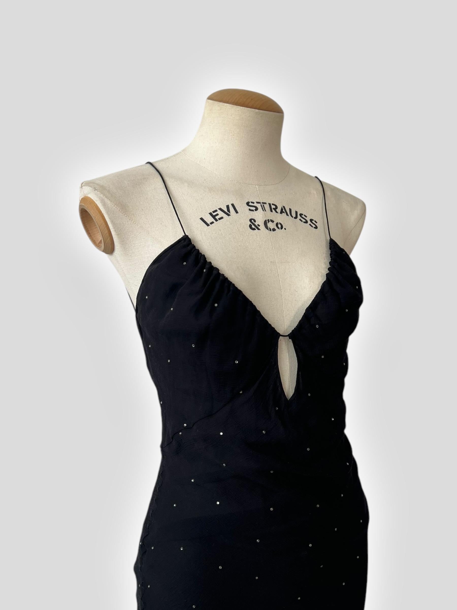 A stunning floor-length gown from Christian Dior by John Galliano, crafted from silk and adorned with delicate rhinestones for a subtle shimmer. The design features a plunging neckline with a keyhole cutout, thin straps, and a body-skimming