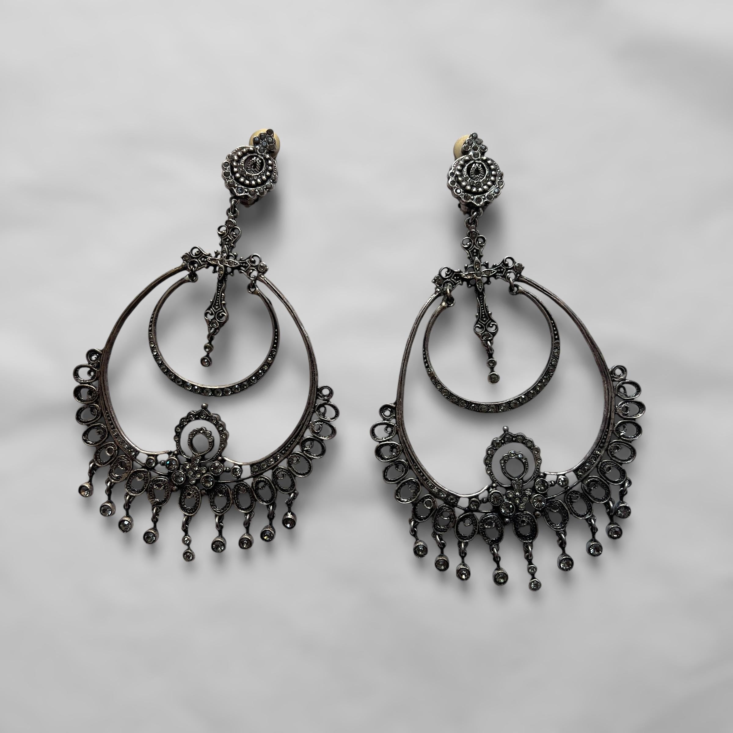 Piece Description: These striking, oversized hoop earrings feature intricate cross details and ornate embellishments, echoing the bold aesthetic of John Galliano's S/S 1999 Dior collection. The earrings exhibit a unique blend of gothic and romantic