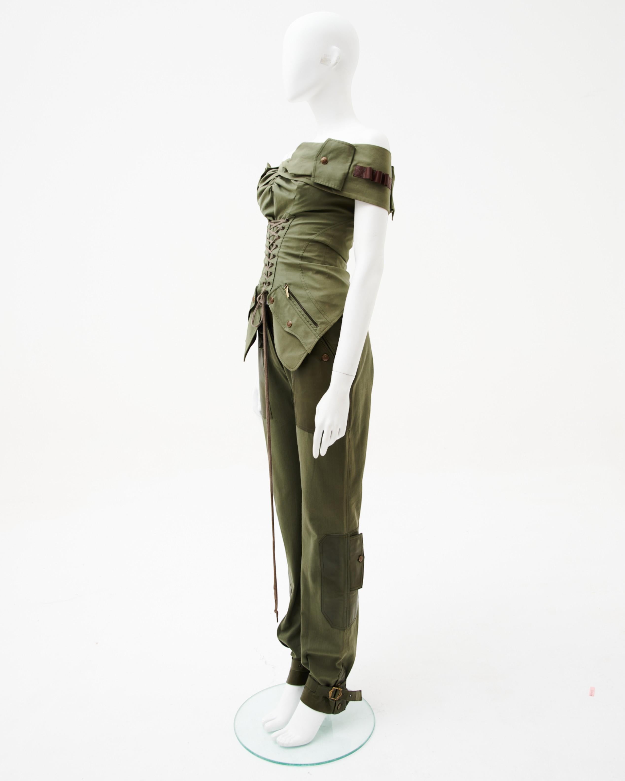 - Entworfen von John Galliano
- Verkauft von Skof.Archive
- Herbst-Winter-Kollektion 2003
- Militärisches Khaki Bondage Set
- Schulterfreies Korsett-Top mit funktionellen Cargotaschen an den Schultern und auf der Vorderseite
- Aufwändige