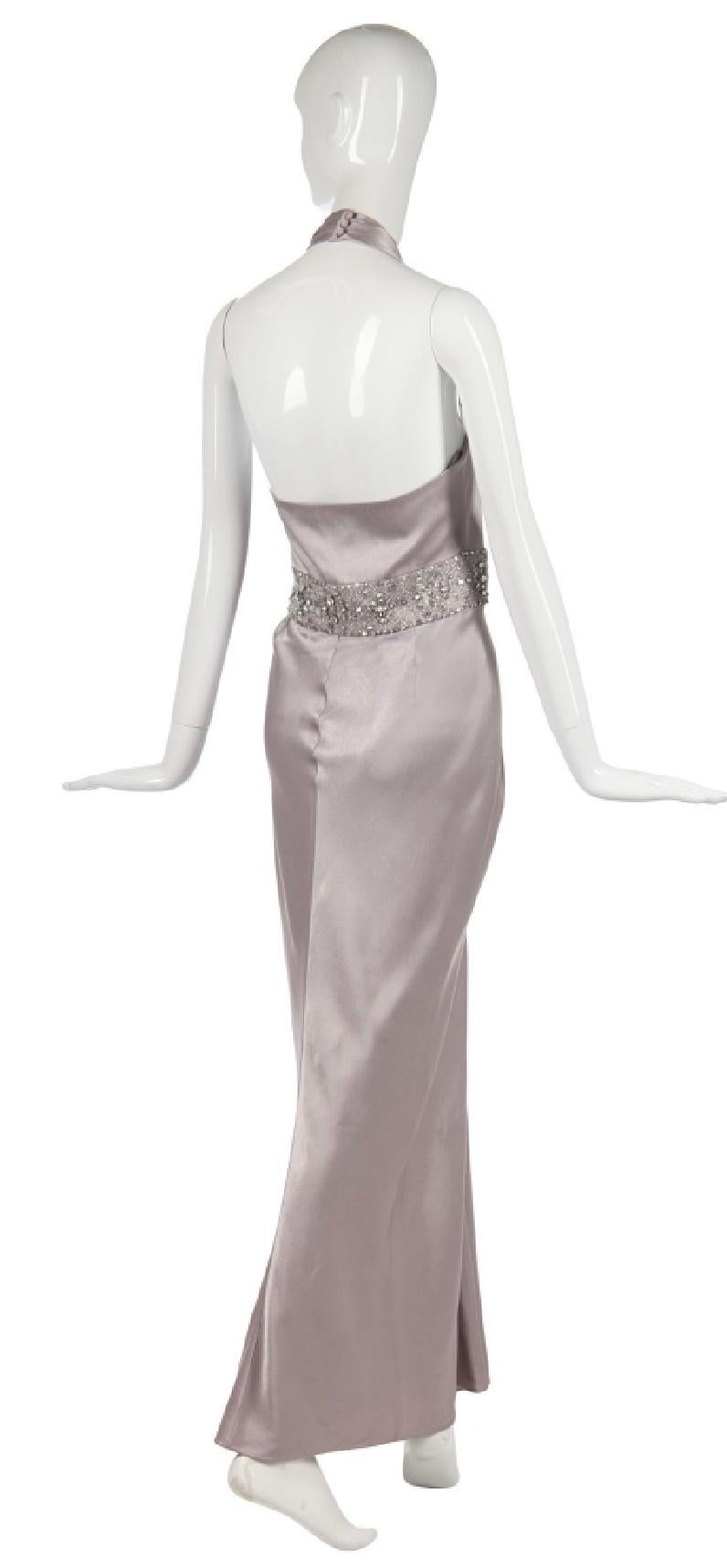 Sumptuous silver satin Christian Dior by John Galliano gown. With elegant pleating, a plunging neckline, and an ornate rhinestone waist, this dress is the height of timeless glamour. Fastens with signature Dior button and loops up the side. 2009. GB