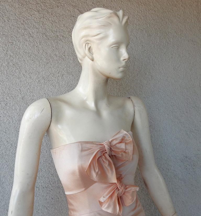 Circa early 2000 John Galliano for the House of Dior strapless blush pink silk bias cut gown.  Fashionably adorned with hand tie bows slightly asymmetric down front of bodice extending down skirt.  Features interior boned bodice with net zipper