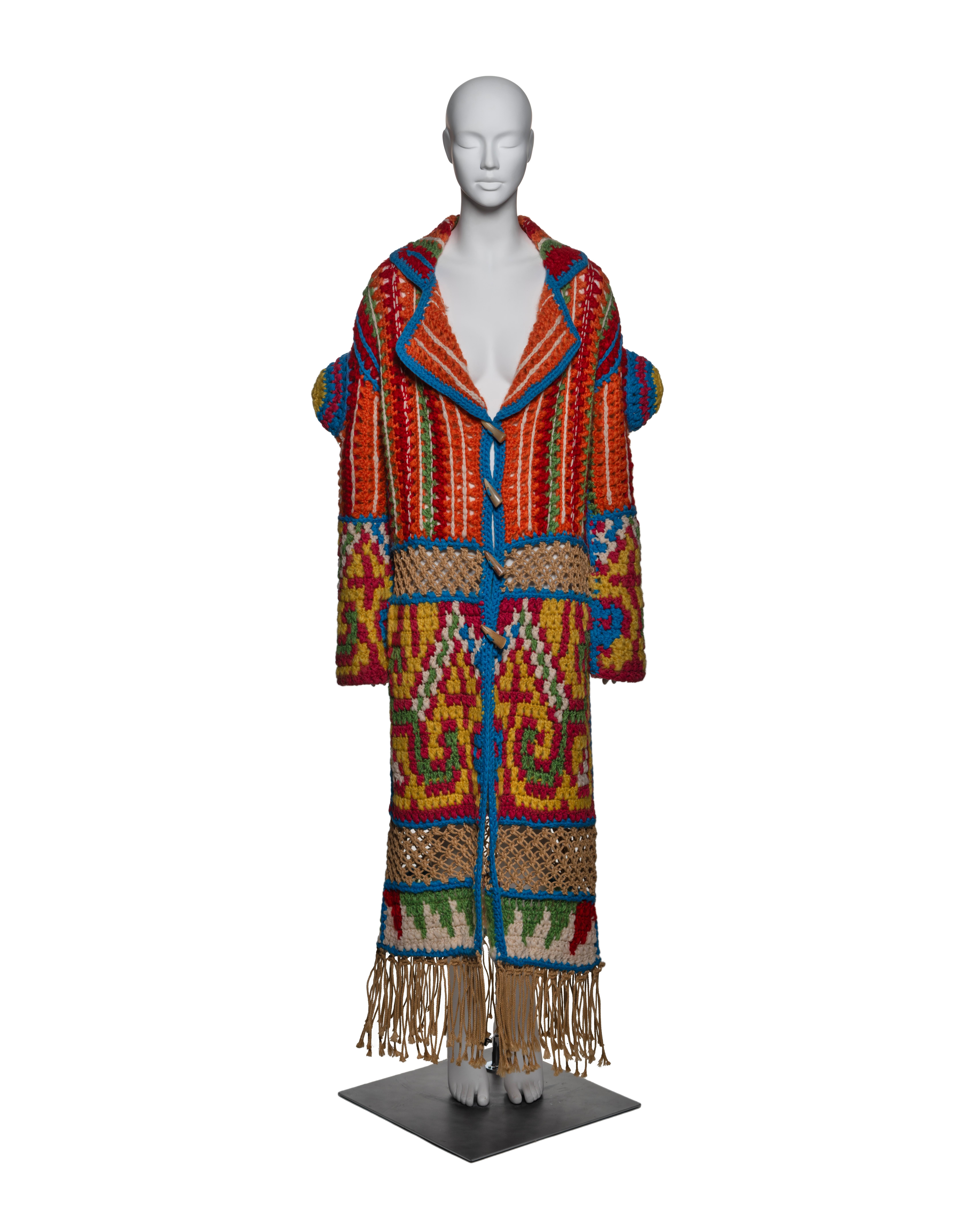 This Christian Dior coat, crafted from mohair, wool, nylon, and jute, features an oversized silhouette with exaggerated, rounded shoulders and a relaxed collar. The coat showcases a hand-crocheted design with vibrant geometric patterns in red,