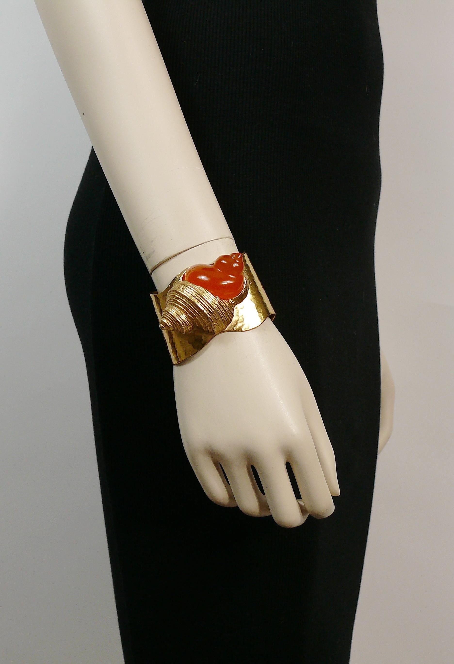 CHRISTIAN DIOR vintage rare hammered gold toned cuff bracelet feautring a large orange resin shell.

Created by French parurier ROBERT GOOSSENS for the launch of the fragrance DUNE in 1987.

Embossed CHRISTIAN DIOR Parfums.

Indicative measurements