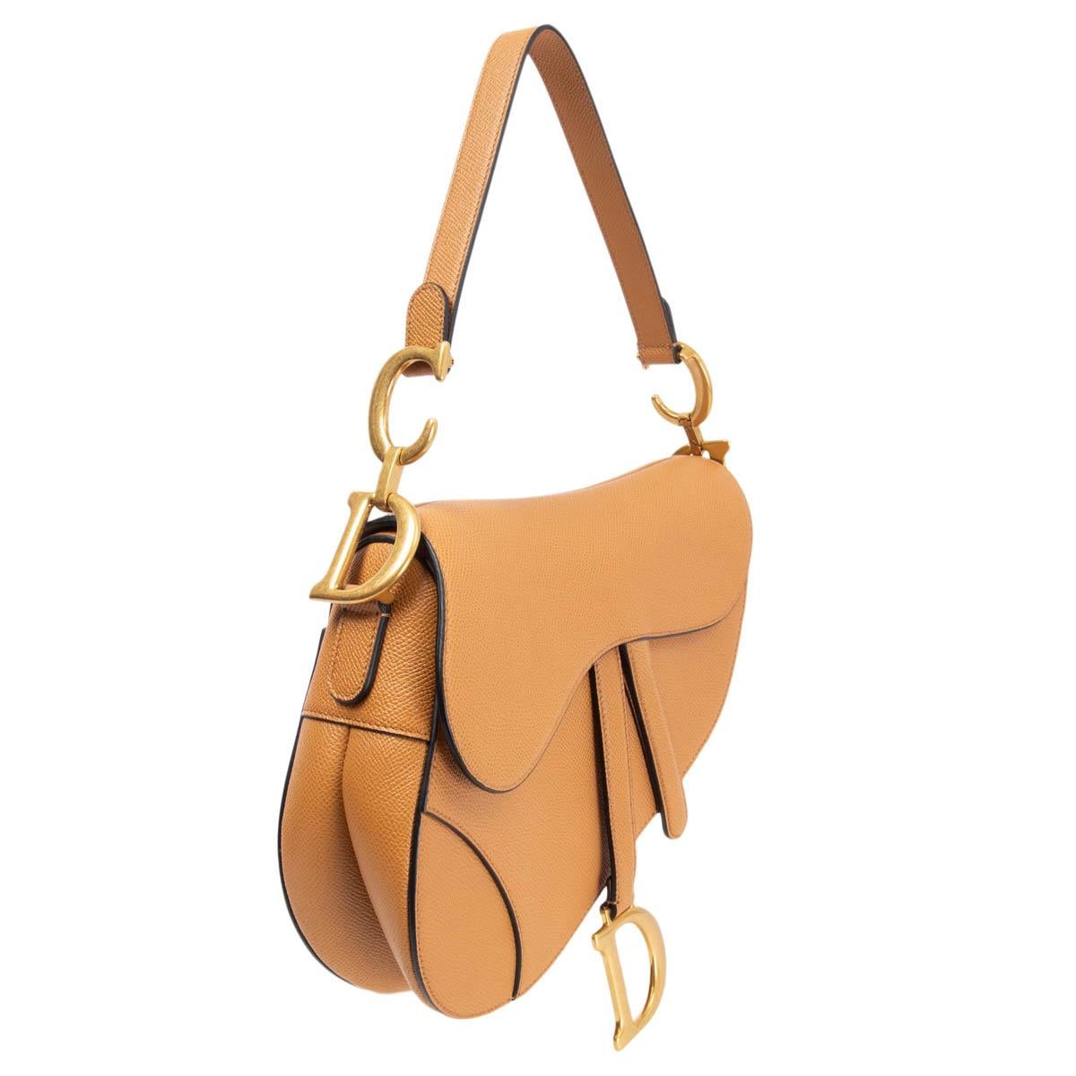 100% authentic Christian Dior Saddle bag in grained camel calfskin with gold-tone CD detail on the strap. The legendary design features a Saddle flap with a magnetic 'D' stirrup clasp, as well as an antique gold-finish metal 'CD' signature on either