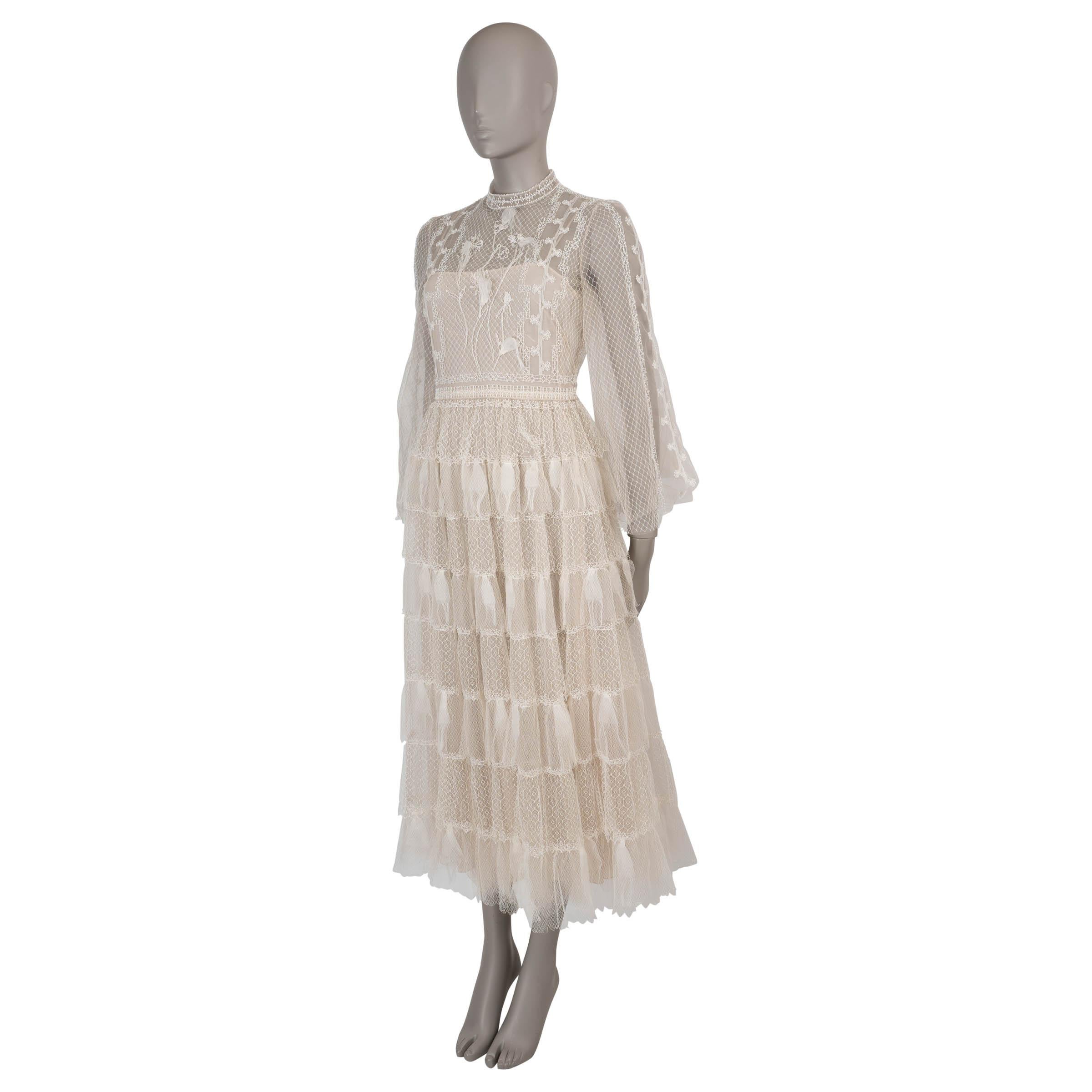 This 100% authentic Christian Dior dress in white tulle is exquisitely adorned with delicate lace, net panels, faux pearl embellishments, and intricate floral embroidery, creating a truly romantic masterpiece. Designed with a relaxed silhouette, it