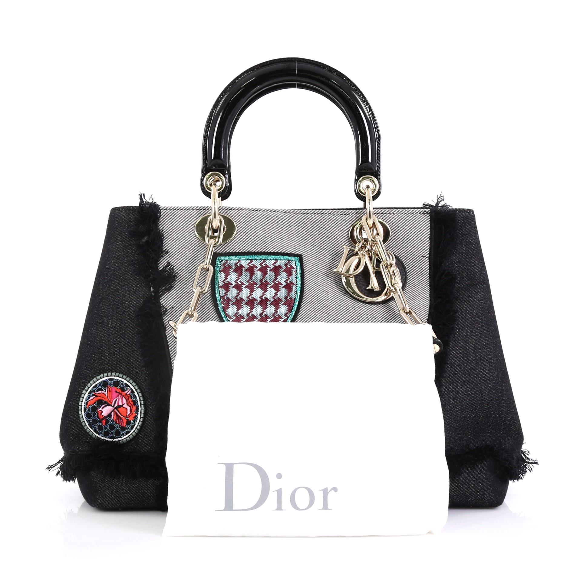 This Christian Dior D-Light Bag Patch Embellished Denim Large, crafted from black embellished denim, features dual top handles, fringe piping, multicolor patches, and gold-tone hardware. Its magnetic snap closure opens to a black denim interior with
