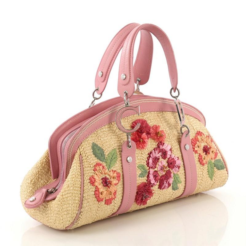 This Christian Dior Detective Doctor Bag Floral Raffia Medium, crafted from multicolor floral raffia, features dual leather handles, raffia flowers on the front, leather trim, and silver-tone hardware. Its zip closure opens to a tan fabric interior