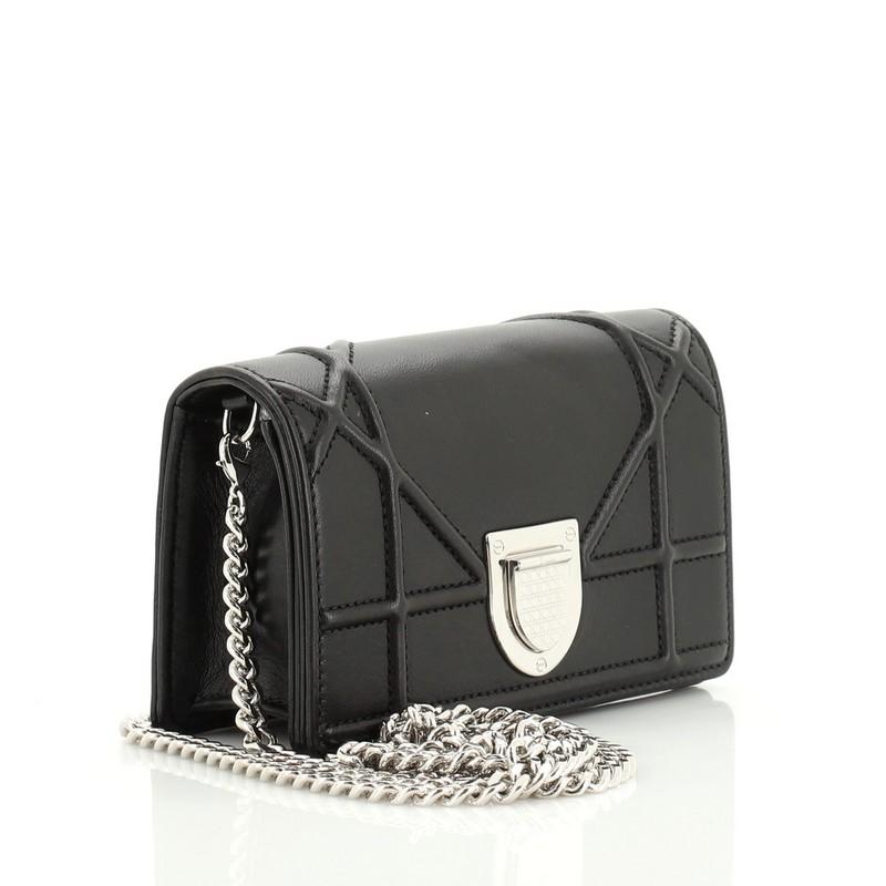 This Christian Dior Diorama Flap Bag Leather Baby, crafted in black calfskin leather, features an oversized cannage quilt design, chain strap with leather pad, and silver-tone hardware. Its crest-shaped clasp closure opens to a black leather
