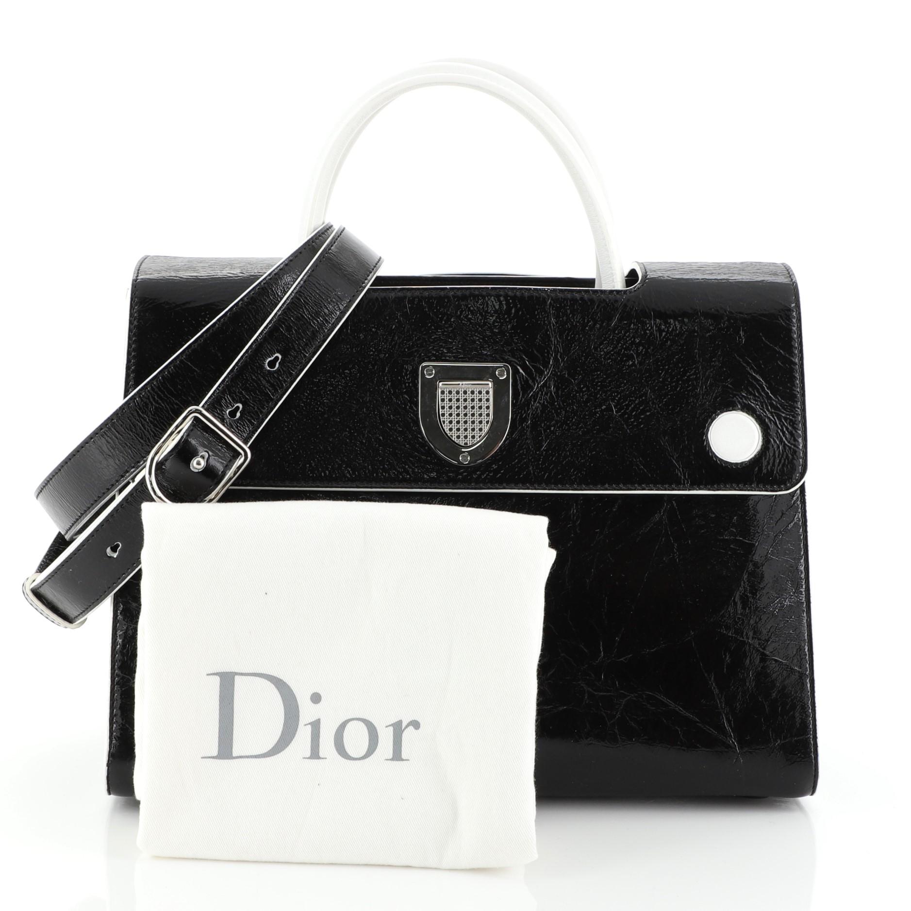 This Christian Dior Diorever Handbag Leather Medium, crafted in black leather, features a reversible flap, dual rolled leather handles, protective base studs and silver-tone hardware. Its crest-shaped clasp closure opens to a black leather interior