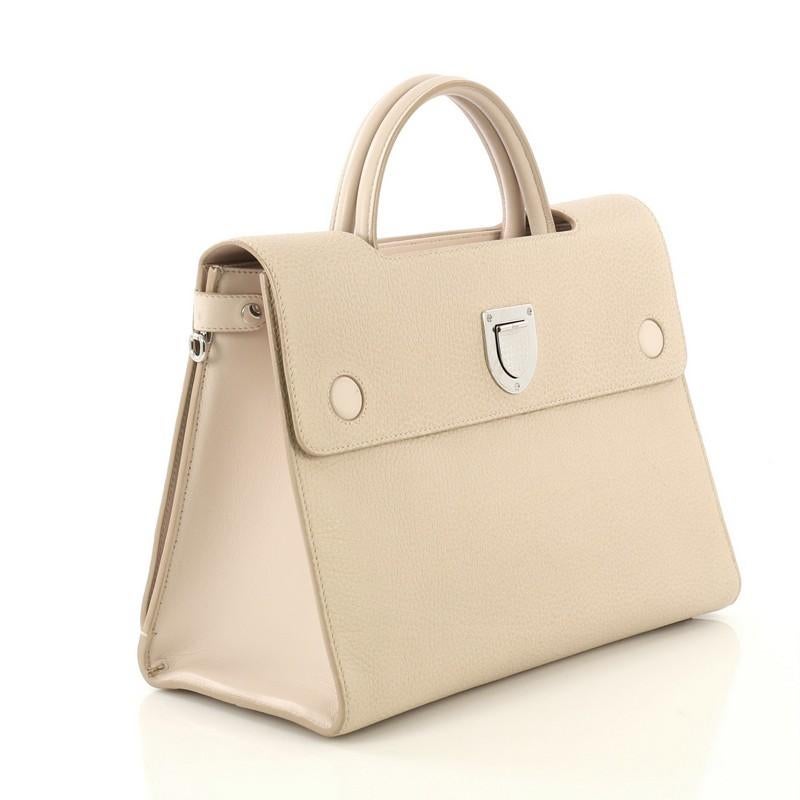 This Christian Dior Diorever Handbag Leather Medium, crafted in neutral leather, features a reversible flap, dual rolled leather handles, protective base studs and silver-tone hardware. Its crest-shaped clasp closure opens to a neutral leather