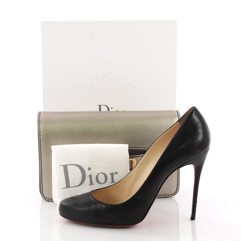 This Christian Dior Dio(r)evolution Clutch Leather Small, crafted from gold metallic leather, features a slot handclasp with gold-tone DIOR emblem and gold-tone hardware. It opens to a taupe suede interior with slip pocket. **Note: Shoe photographed