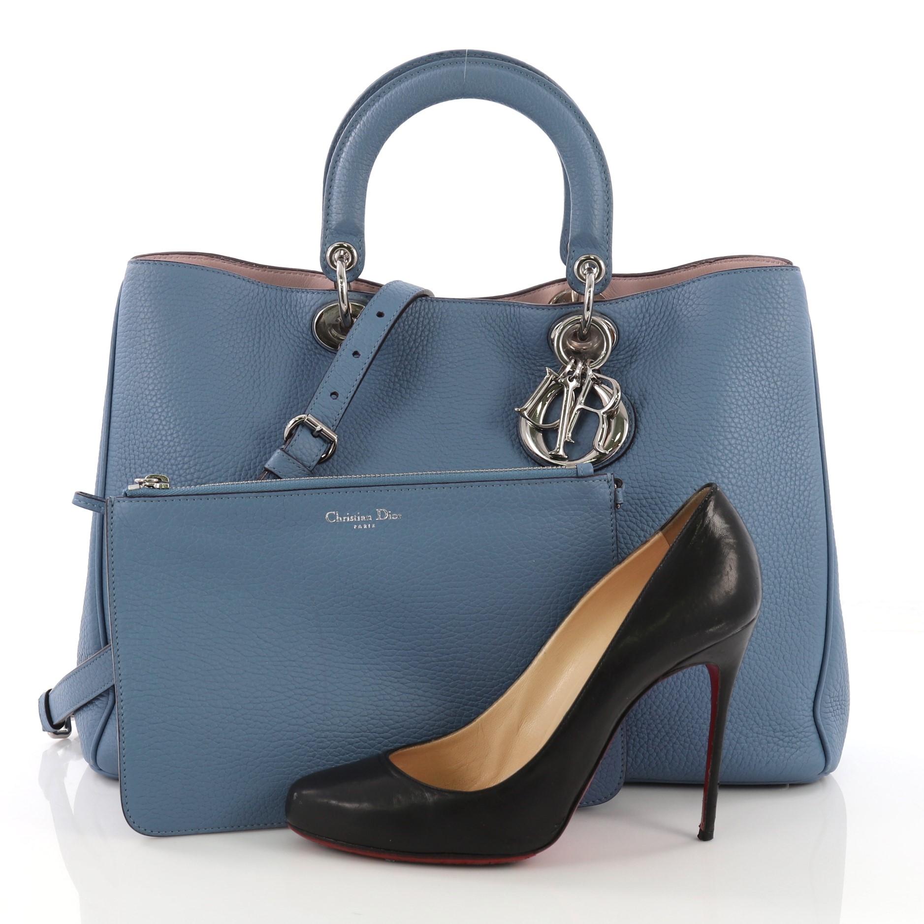 This Christian Dior Diorissimo Tote Pebbled Leather Large, crafted from blue pebbled leather, features smooth short dual handles with sleek Dior charms, side snap buttons, and silver-tone hardware. Its magnetic snap closure opens to a lavendar