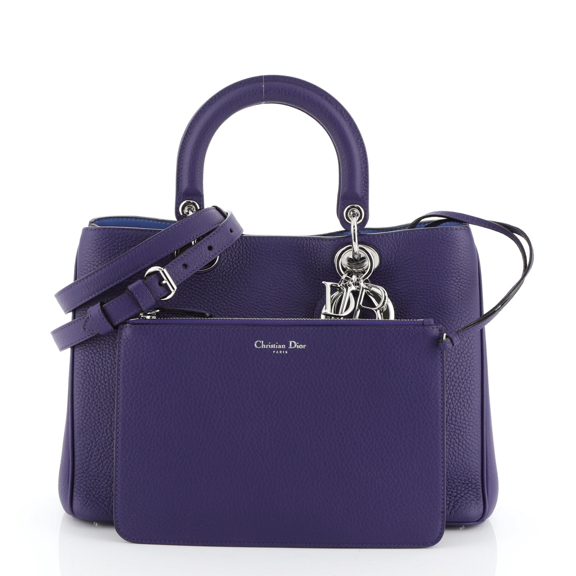 This Christian Dior Diorissimo Tote Pebbled Leather Medium, crafted from purple pebbled leather, features short dual handles with Dior charms, side snap buttons, protective base studs, and silver-tone hardware. Its magnetic snap button closure opens