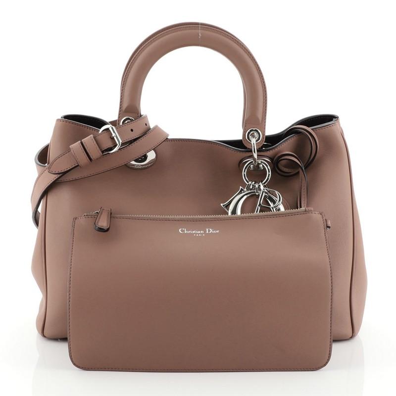 This Christian Dior Diorissimo Tote Smooth Calfskin Medium, crafted in pink smooth leather, features short dual handles with Dior charms, side snap buttons, protective base studs and silver-tone hardware. Its magnetic snap closure opens to a purple