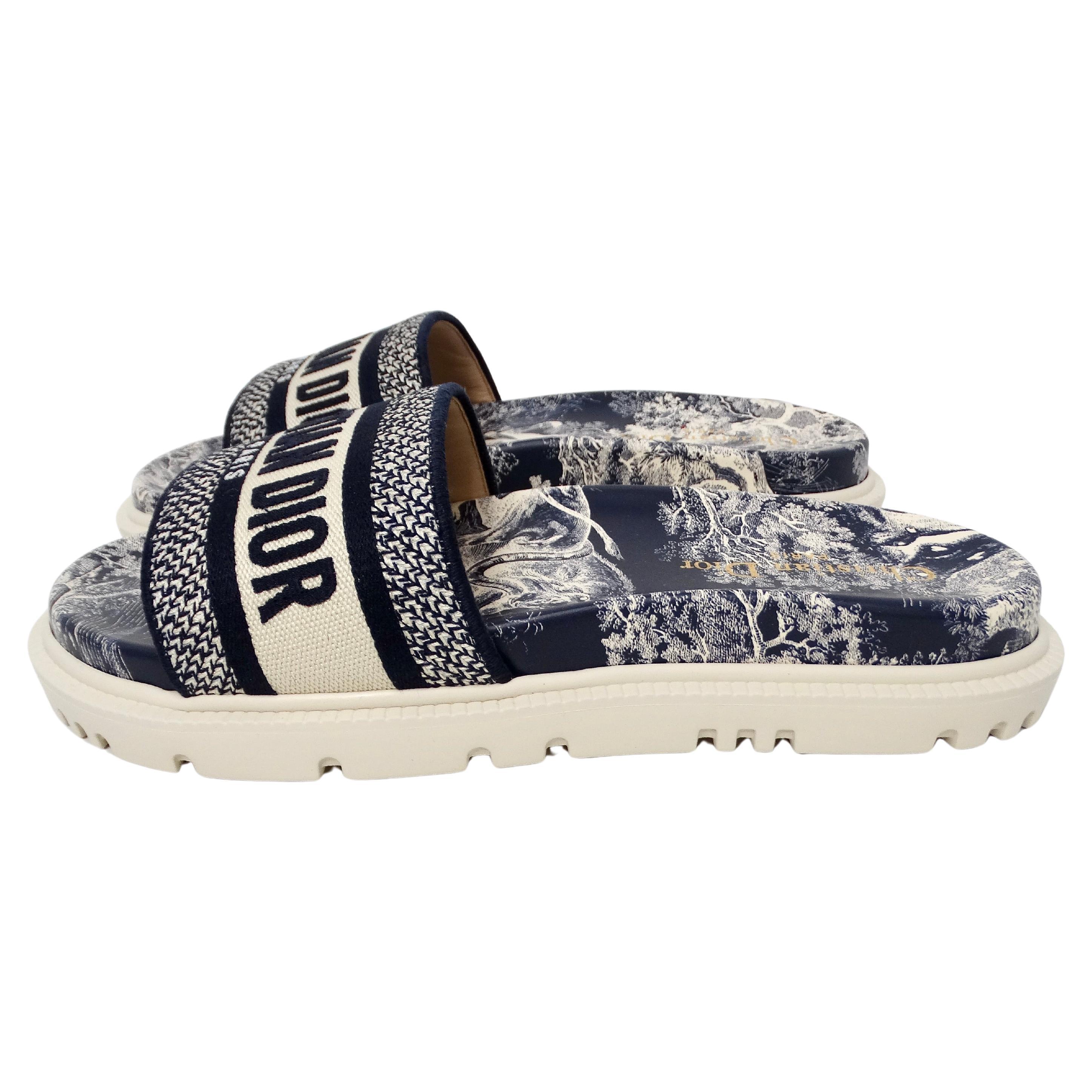 The Christian Dior Dway Canvas Toile de Jouy Blue Embroidered Slides are a luxurious and stylish footwear choice that seamlessly blends classic elegance with contemporary design. Crafted with high-quality canvas featuring the iconic Toile de Jouy