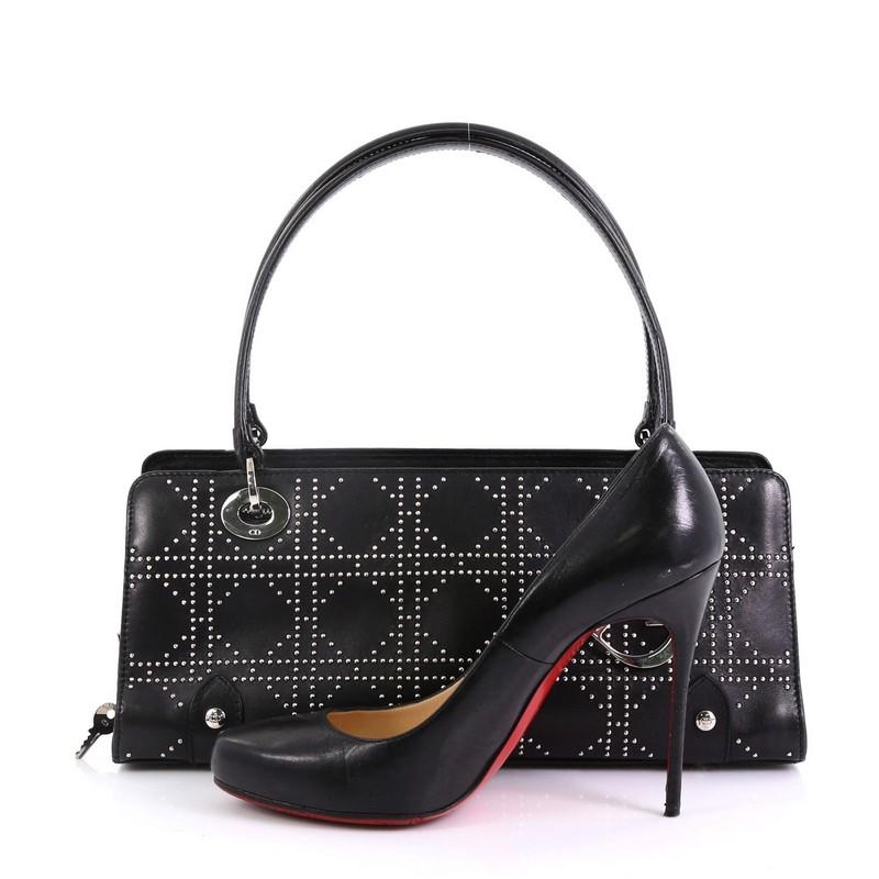 This Christian Dior East West Lady Dior Handbag Cannage Studded Leather Small, crafted from black studded cannage leather, features dual flat leather handles with links, protective base studs, and silver-tone hardware. Its zip closure opens to a red