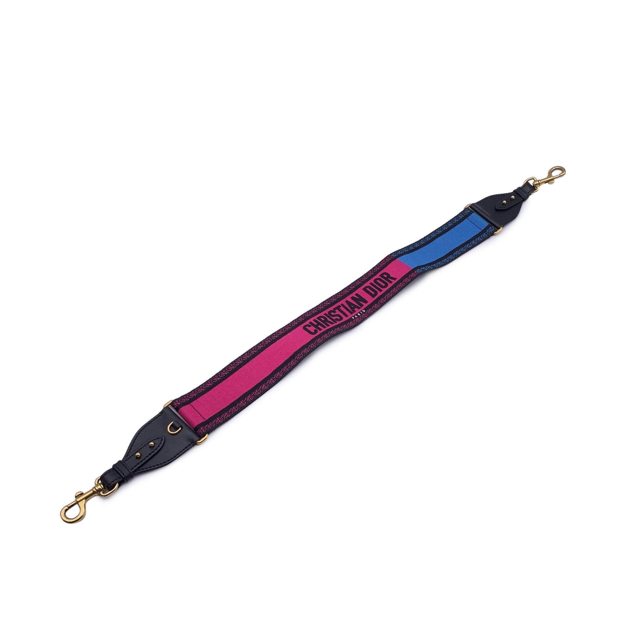 Christian Dior canvas adjustable shoulder strap in fuchsia, blue and black colors. It is embellished with the Christian Dior Paris signature in the center, and it features black leater at the ends. Gold metal Carabiner hooks. A metal ring on leather