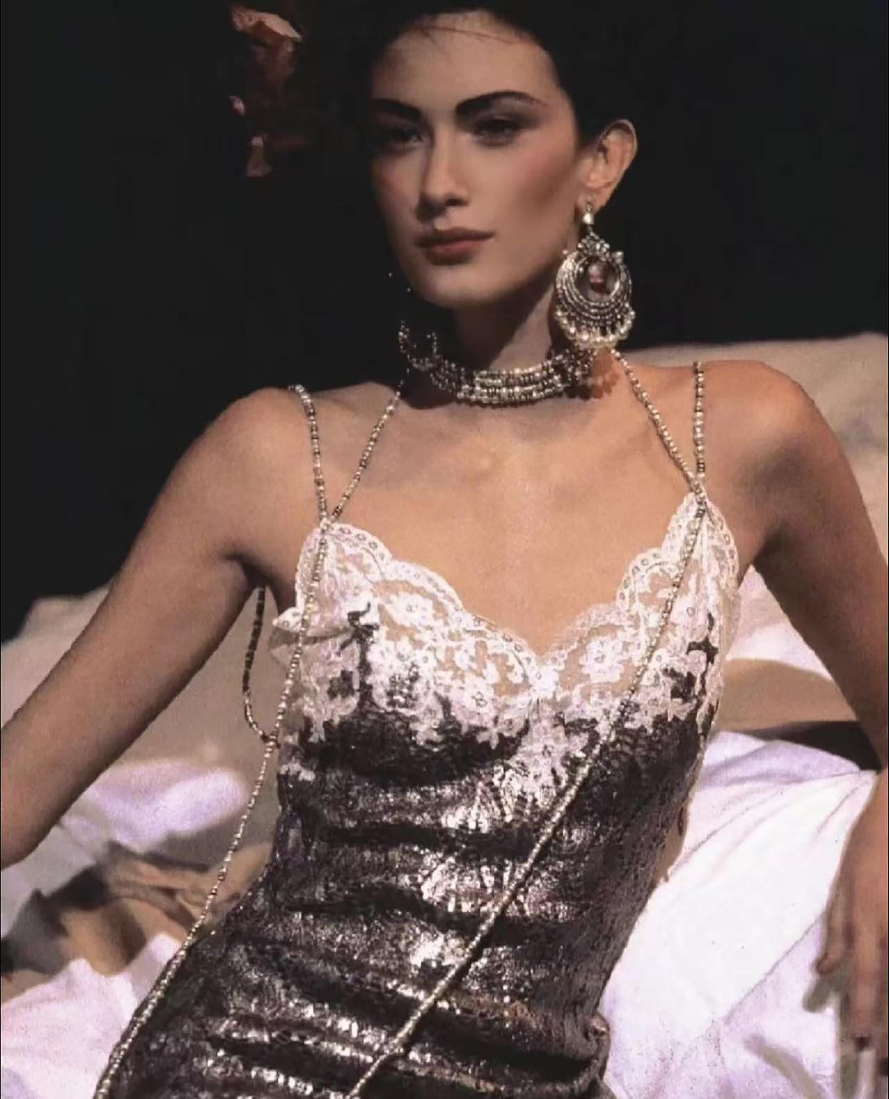 Dieses elegante, anthrazitfarbene Kleid hat eine taillierte Silhouette mit einem raffinierten, quadratischen Ausschnitt, der mit einer zarten Spitzenborte verziert ist. Das herausragende Detail sind die einzigartigen Perlenbänder, die dem Design