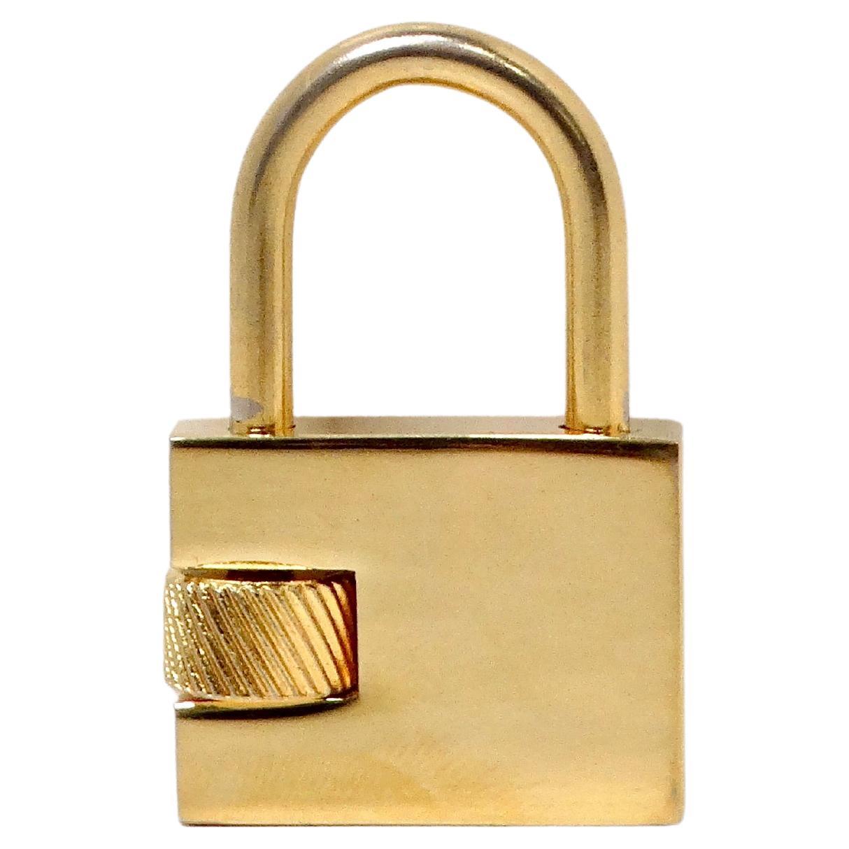 The Christian Dior Gold-Tone Logo Engraved Padlock Charm Pendant is a sophisticated and stylish accessory that seamlessly combines luxury with practicality. Crafted in a radiant gold-tone finish, this charm features the iconic Dior logo engraved