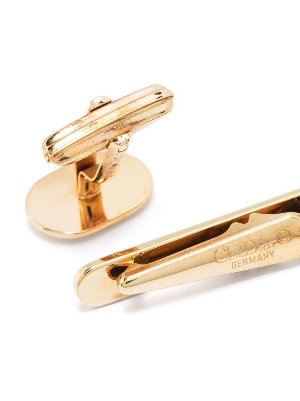 Goldfarbenes Manschettenknöpfe- und Krawattenklammer-Set von Christian Dior mit ovalem Logo-Stempel, Drehverschluss und polierter Oberfläche. 
Die  Krawattenspange  mit Clipverschluss, geprägtem Logo auf der Vorderseite und eingraviertem Logo auf