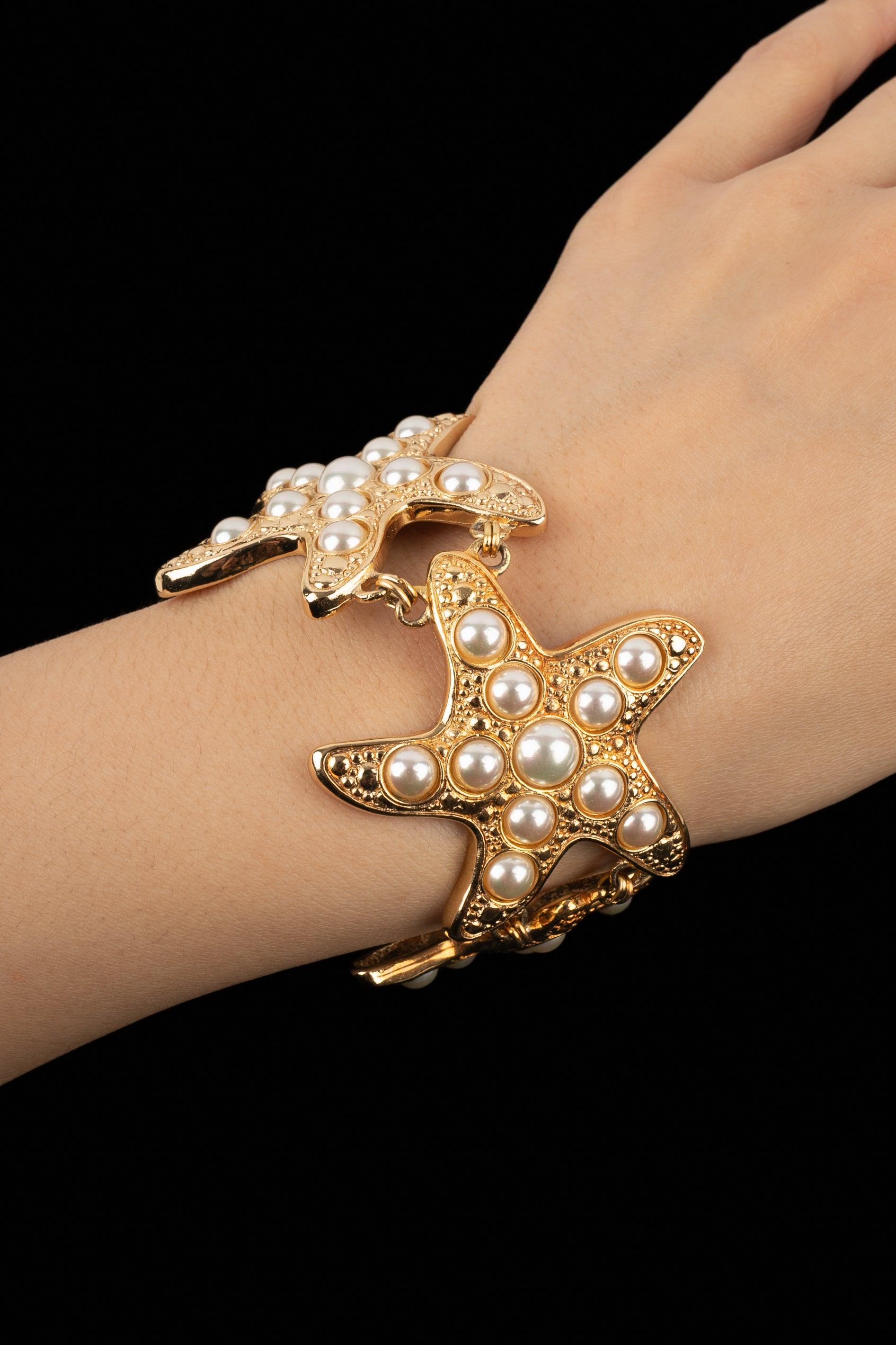 Dior - Golden metal articulated bracelet representing starfishes decorated with pearly cabochons.

Additional information:
Condition: Very good condition
Dimensions: Length: 20 cm

Seller Reference: BRA145