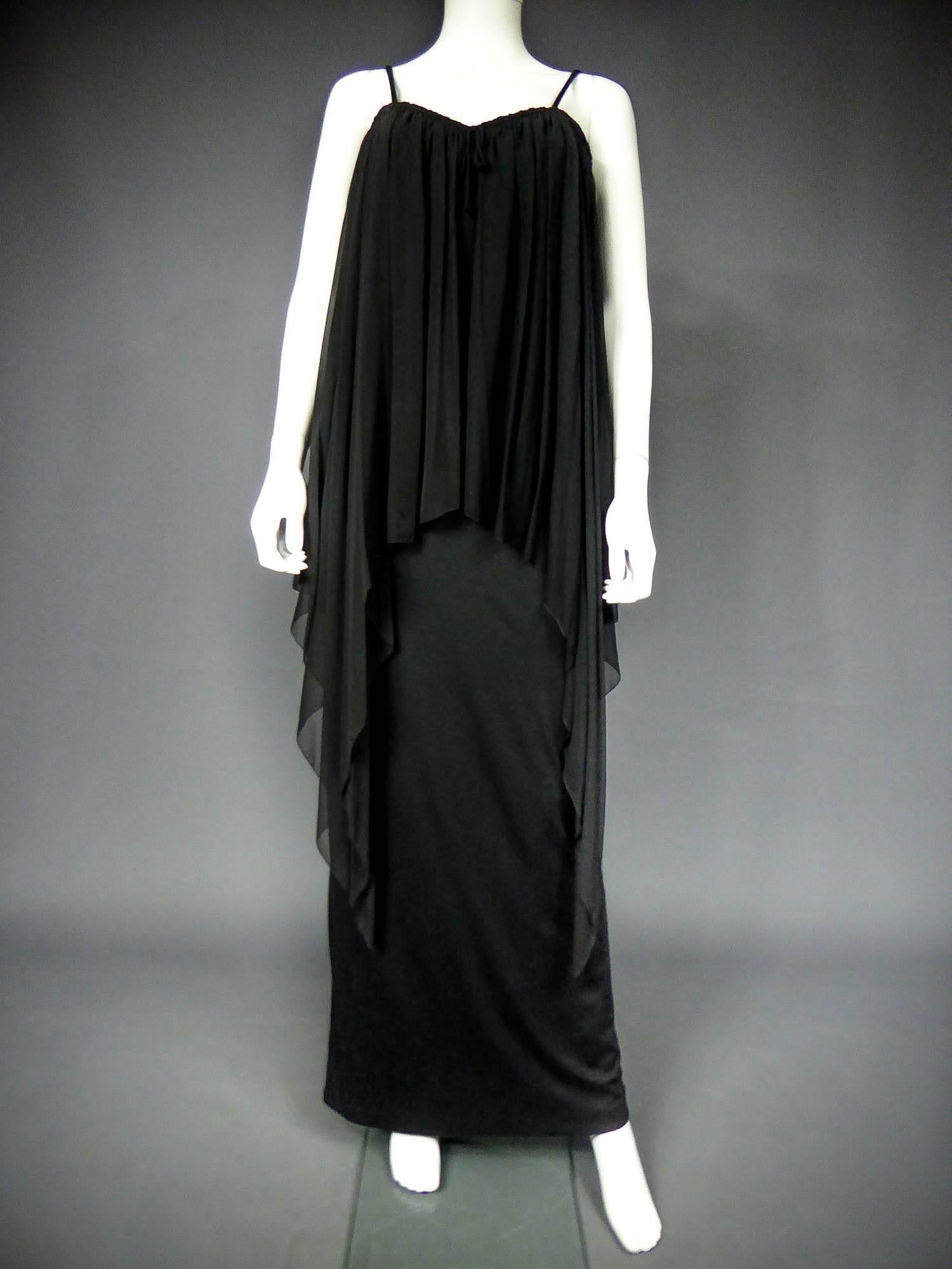 Circa 1975

France

Long bat dress in jersey and silk muslin tightened at the chest by a tie. Sleeveless low-cut neckline retained by fine matching straps. Huge asymmetrical triangle with a pointed cut in bias and hands finishes. Cape effect