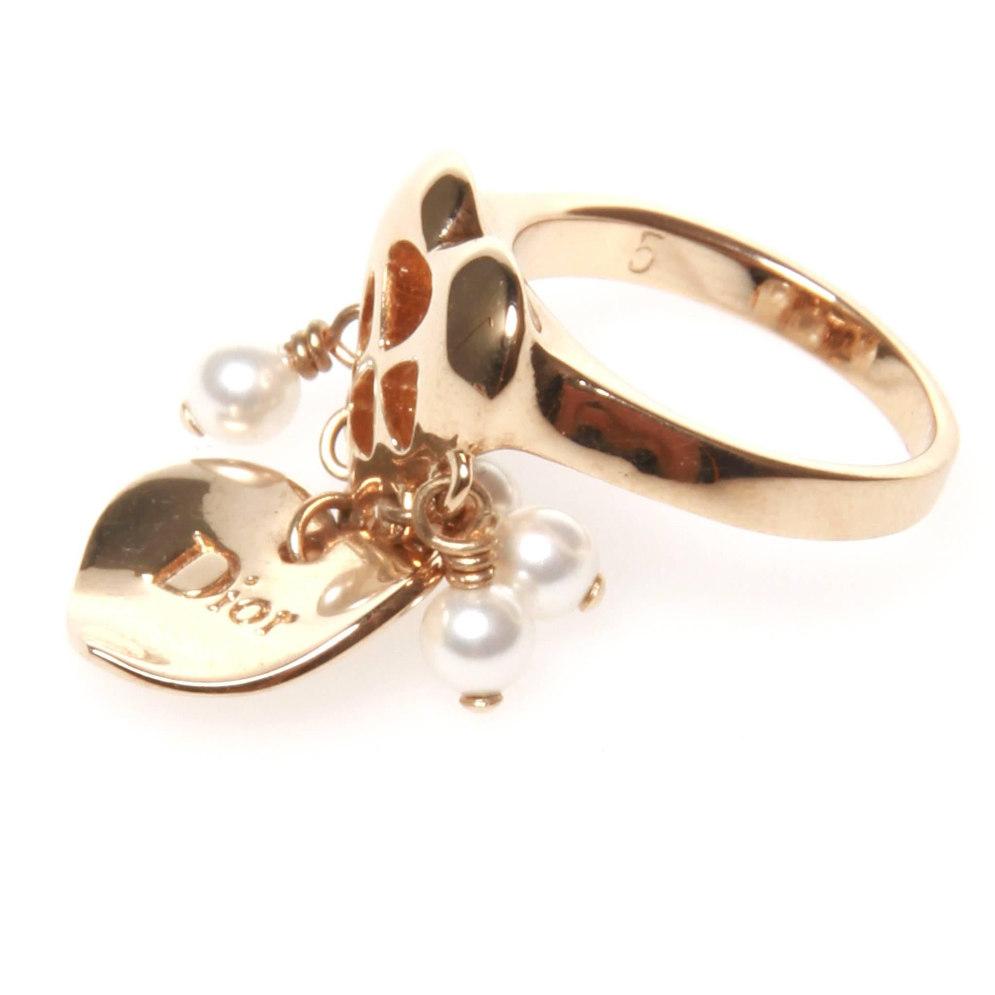 Christian Dior ring in gold-tone metal featuring a cut-out love heart with dangling love heart and faux pearl charms. 

Size 5. With original box. 