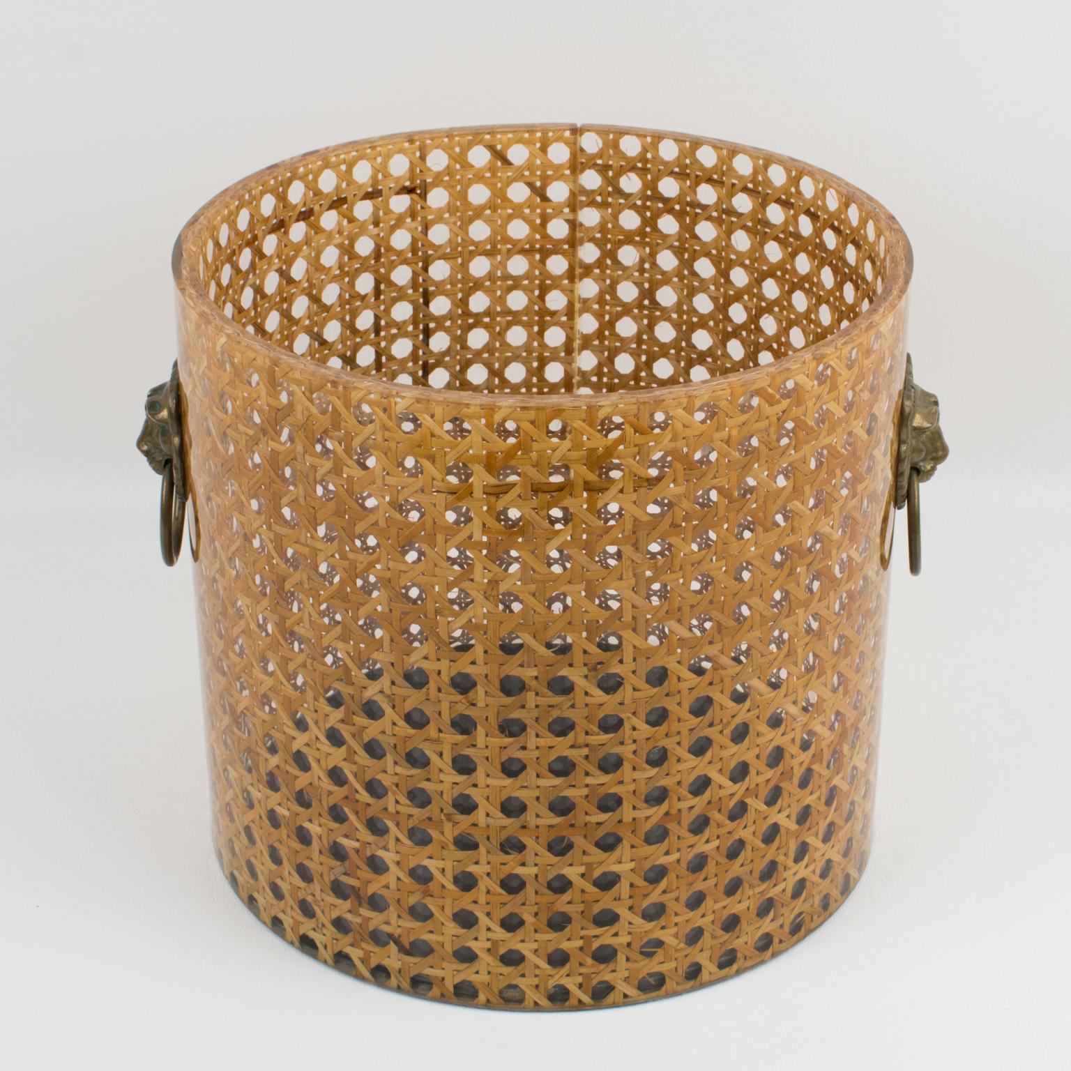 Lovely wastebasket or planter designed by Christian Dior for his Home Collection in the 1970s. Rounded shape with real rattan cane work embedded in the crystal clear Lucite. Two brass handles on sides with lion head carving and ring. Great desk or