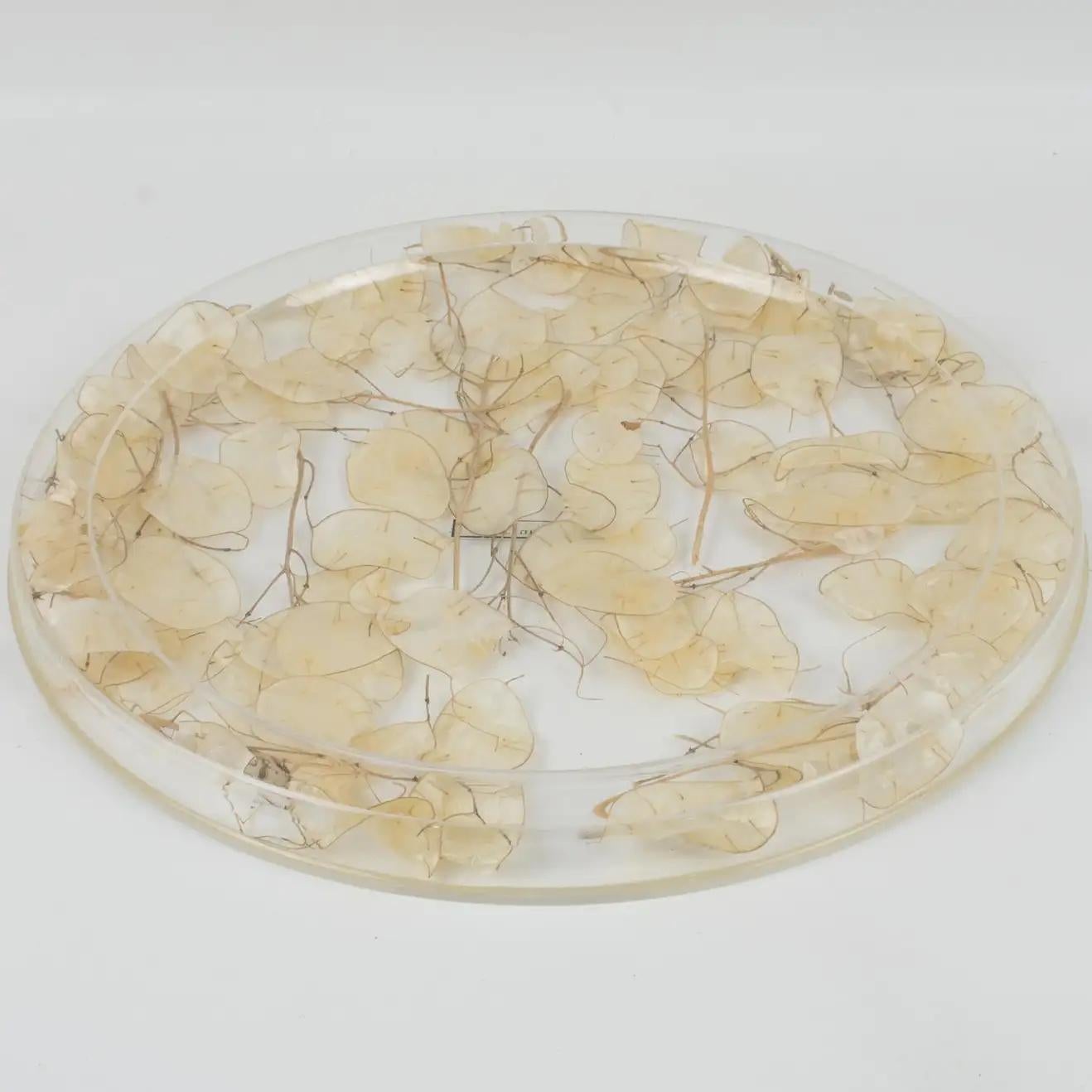 This is a lovely serving tray designed by Christian Dior in the 1970s for his Home Collection. This board or platter has a rounded shape and raised edges. With a natural organic touch, it is made of clear Lucite or plexiglass with real dried Lunaria