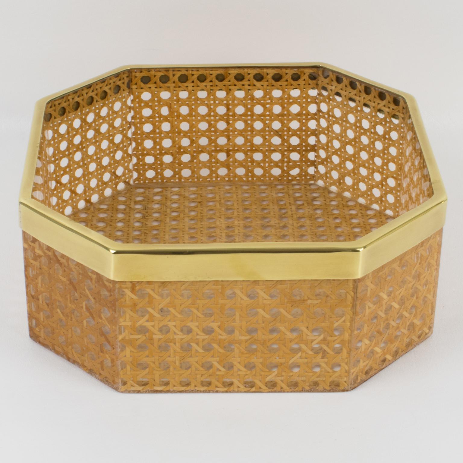 Esta impresionante cesta o cuenco decorativo fue diseñada para la colección Christian Dior Home hacia 1970. Su forma geométrica tiene una galería metálica de latón y auténticos trabajos de mimbre o ratán incrustados en el Lucite cristalino. Es un