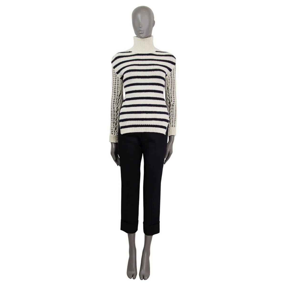 This 100% authentic Christian Dior Marinière sweater in off-white and navy blue striped wool (70%) and polyamide (30%) reimagines the classic nautical style with a modern, feminine twist. Featuring a cozy turtleneck and long chunky knit sleeves, it