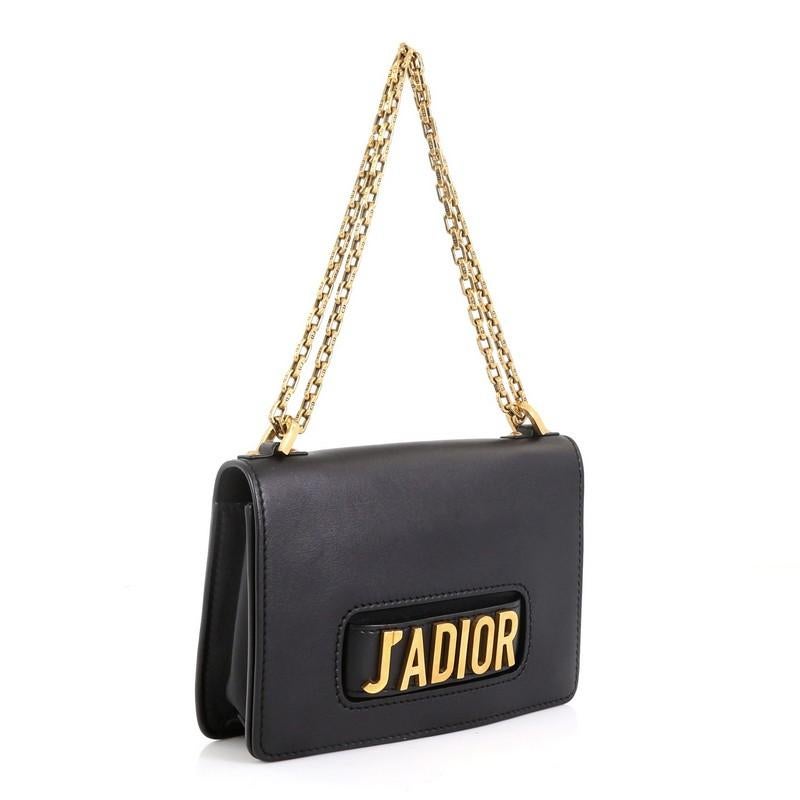This Christian Dior J'adior Flap Bag Calfskin Medium, crafted in black leather, features a slot handclasp with metal plated J'adior signature, chain link strap, full front flap and aged gold-tone hardware. It opens to a black suede interior with