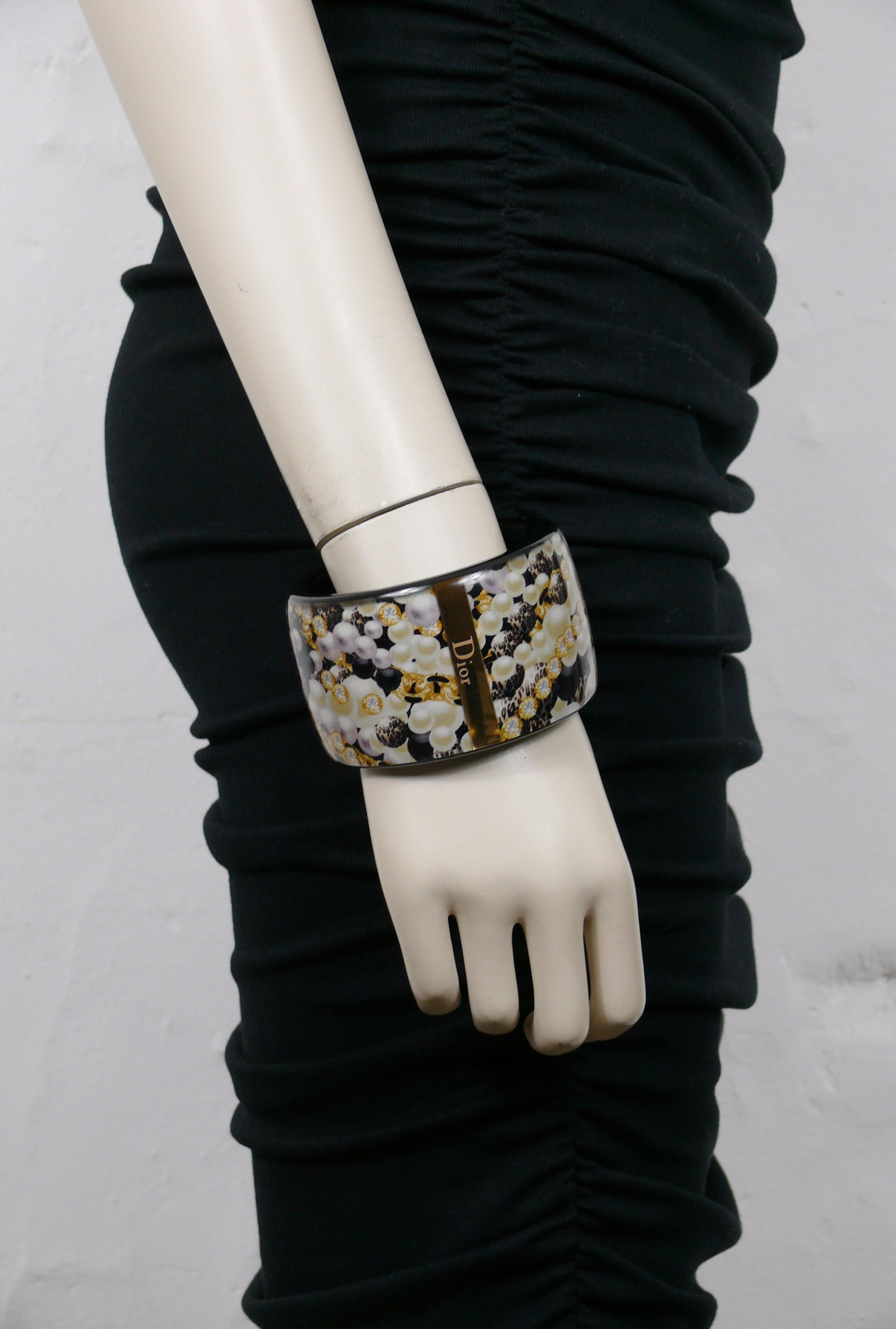 CHRISTIAN DIOR black resin cuff bracelet featuring a jewelry print (pearls, crystals, brooch) inlaid.

Embossed DIOR on a gold tone metal inlaid.

Indicative measurements : inner circumference approx. 20.42 cm (8.04 inches) / width approx. 4.9 cm