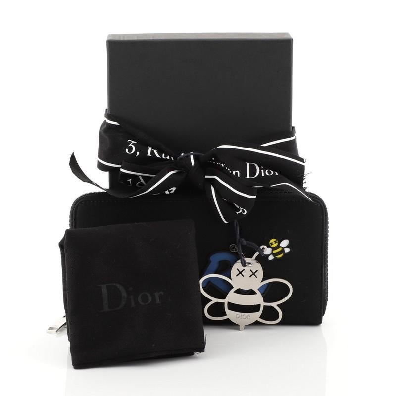 This Christian Dior KAWS Zip Around Wallet Nylon with Applique, crafted from black nylon, features Dior logo and bee applique and silver-tone hardware. Its zip closure opens to a black leather interior with zip and slip pockets. 

Estimated Retail