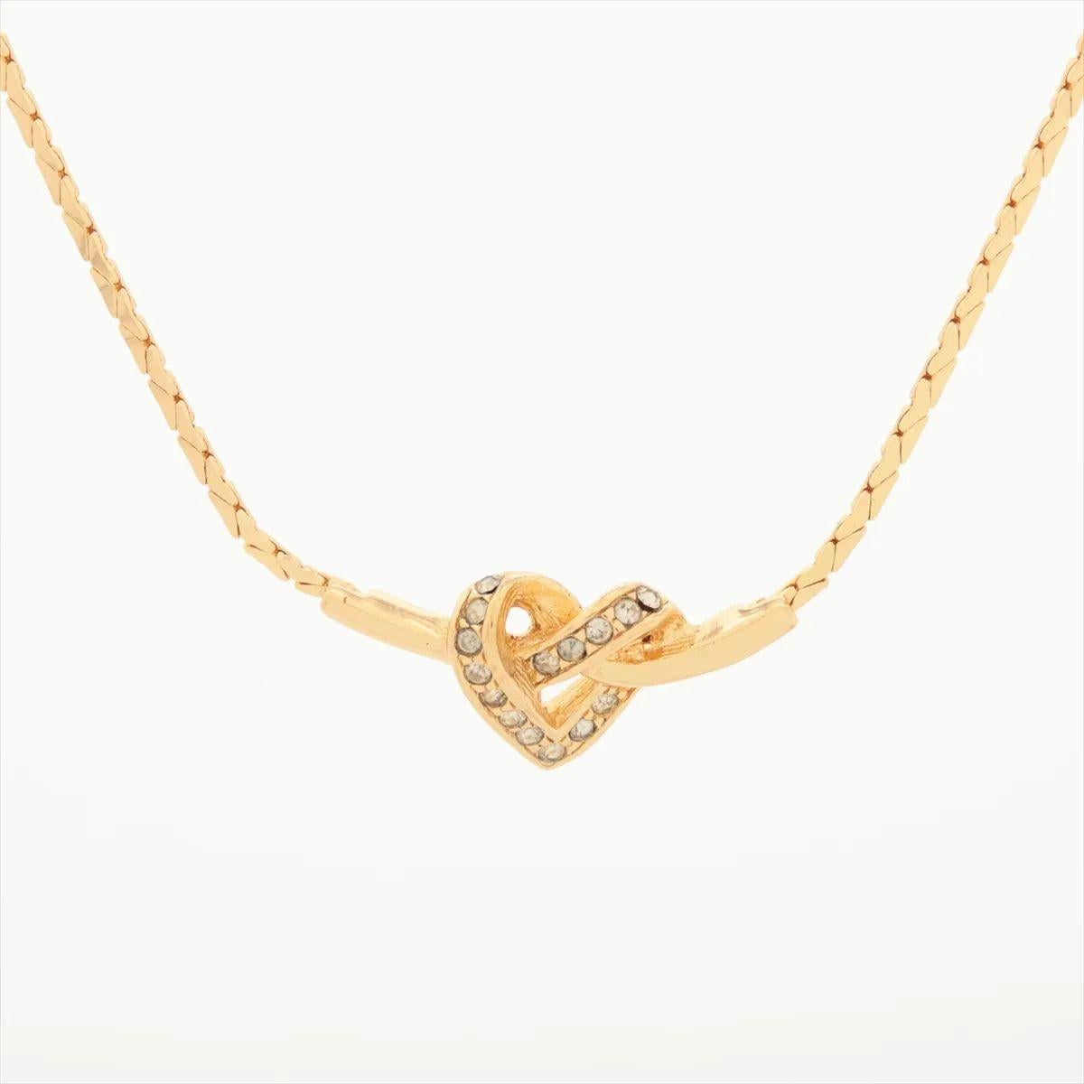 Die goldfarbene Christian Dior Knot Heart Strass-Halskette ist ein romantisches und elegantes Accessoire, das Charme mit Raffinesse verbindet. Der herzförmige Anhänger ist mit schimmernden Strasssteinen besetzt und wird von einem anmutigen