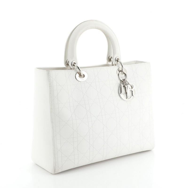 This Christian Dior Lady Dior Bag Stitched Cannage Leather Large, crafted from white stitched cannage leather, features dual top handles and silver-tone hardware. It opens to a brown fabric interior with zip pocket. 

Condition: Fair. Odor in