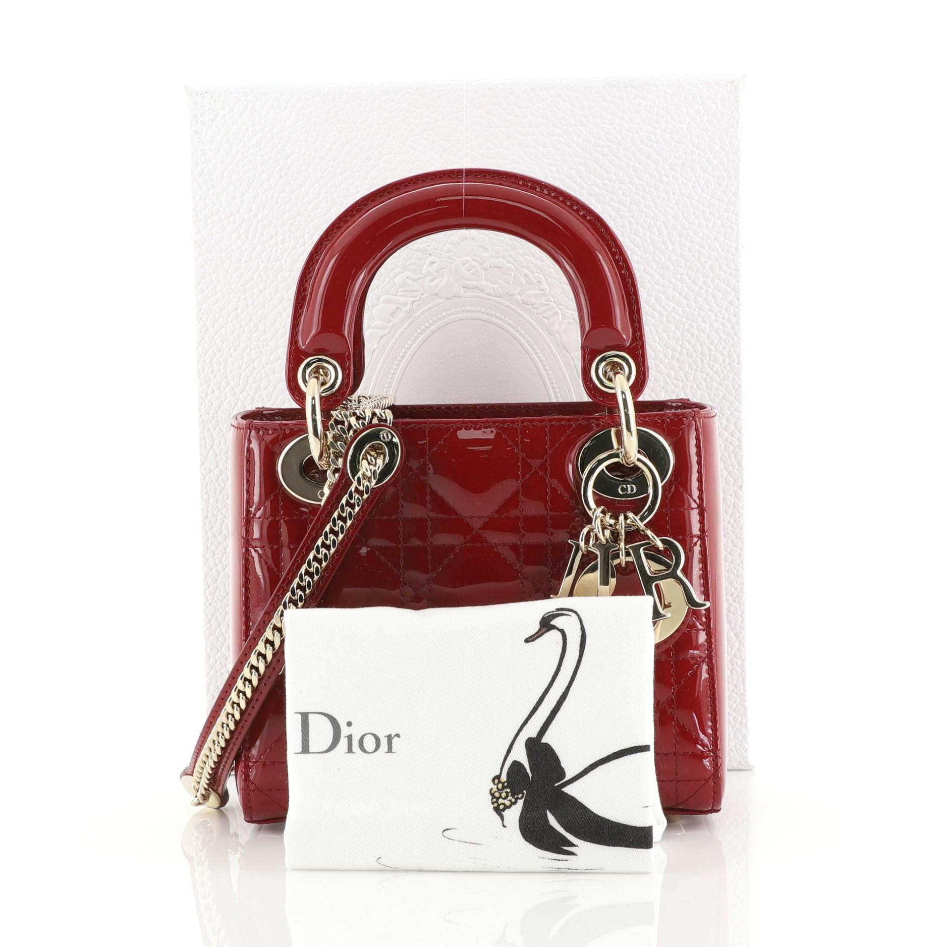 This Christian Dior Lady Dior Chain Bag Cannage Quilt Patent Mini, crafted in red cannage quilted patent leather, features dual top leather handles, detachable chain link strap, protective base studs, and gold-tone hardware. It opens to a red fabric