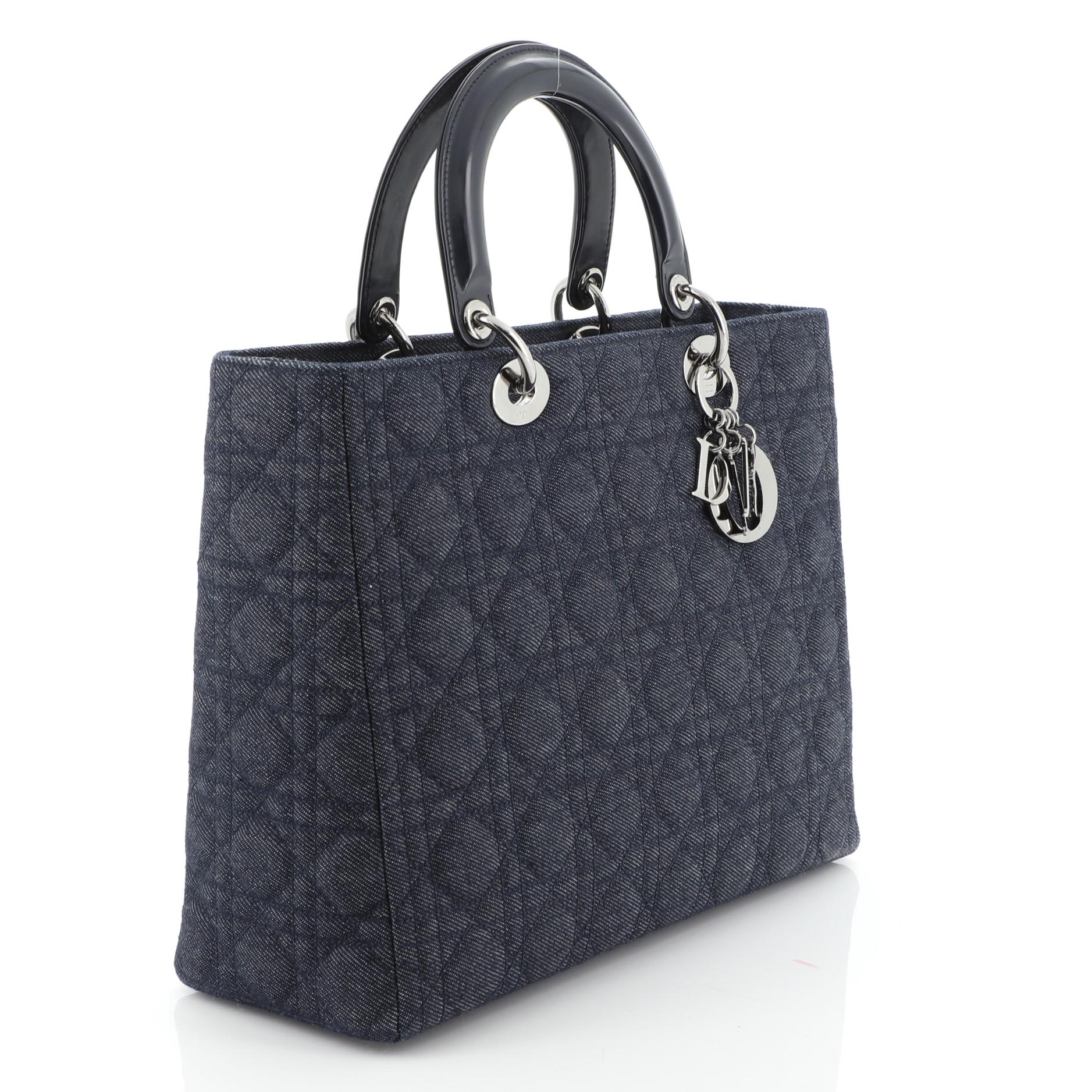 This Christian Dior Lady Dior Handbag Cannage Quilt Denim Large, crafted from blue denim, features short dual handles with sleek Dior charms, protective base studs, and gunmetal-tone hardware. Its top zipper closure opens to a blue fabric interior