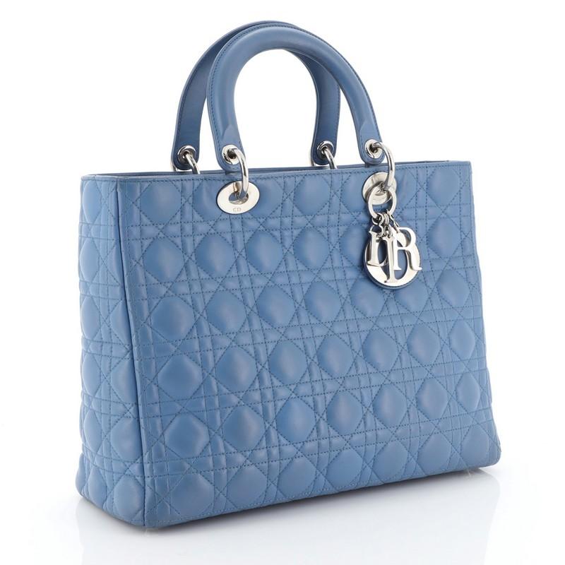 This Christian Dior Lady Dior Handbag Cannage Quilt Lambskin Large, crafted in blue cannage quilted lambskin leather, features short dual handles with Dior charms and silver-tone hardware. Its top zip closure opens to a gray fabric interior with zip