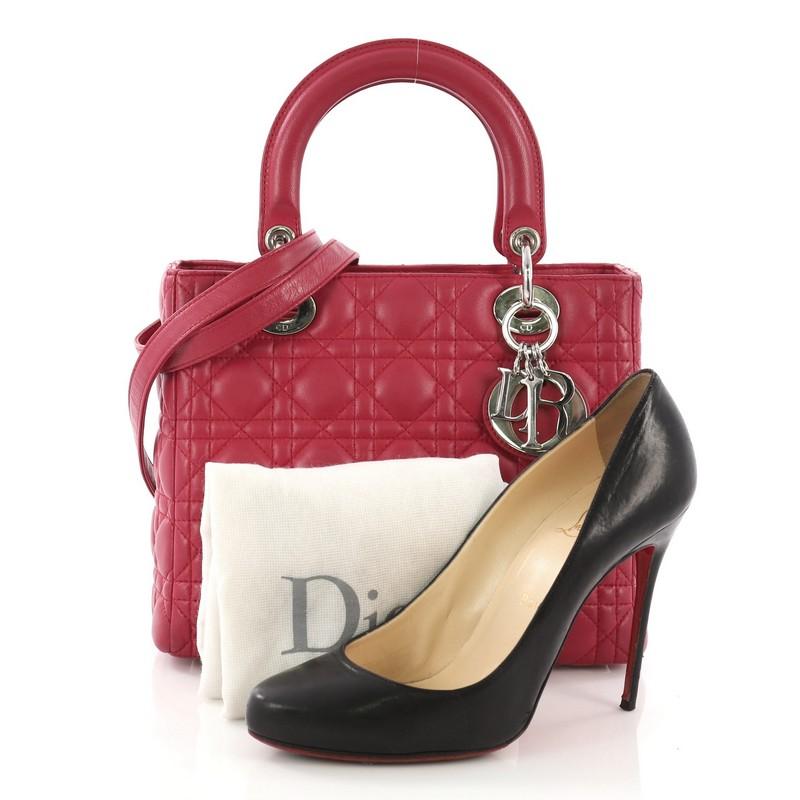 This Christian Dior Lady Dior Handbag Cannage Quilt Lambskin Medium, crafted in dark pink cannage quilt lambskin, features dual top leather handles, Dior charms, protective base studs, and silver-tone hardware. Its zip closure opens to a gray fabric