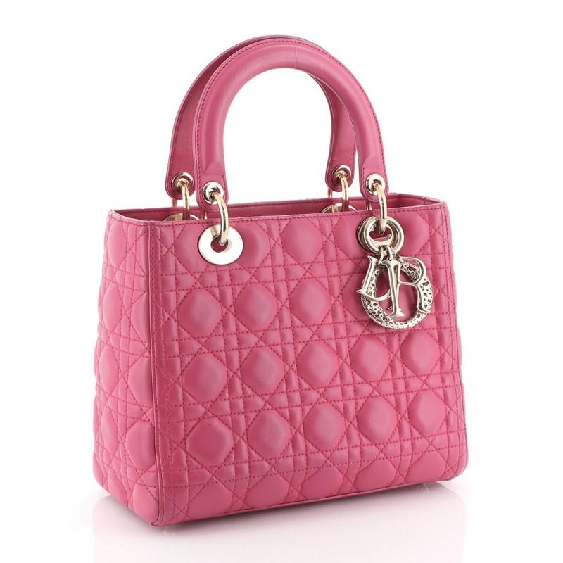 This Christian Dior Lady Dior Handbag Cannage Quilt Lambskin Medium, crafted in pink cannage quilted lambskin leather, features short dual handles with Dior charms and gold-tone hardware. Its zip closure opens to a purple multicolor printed fabric