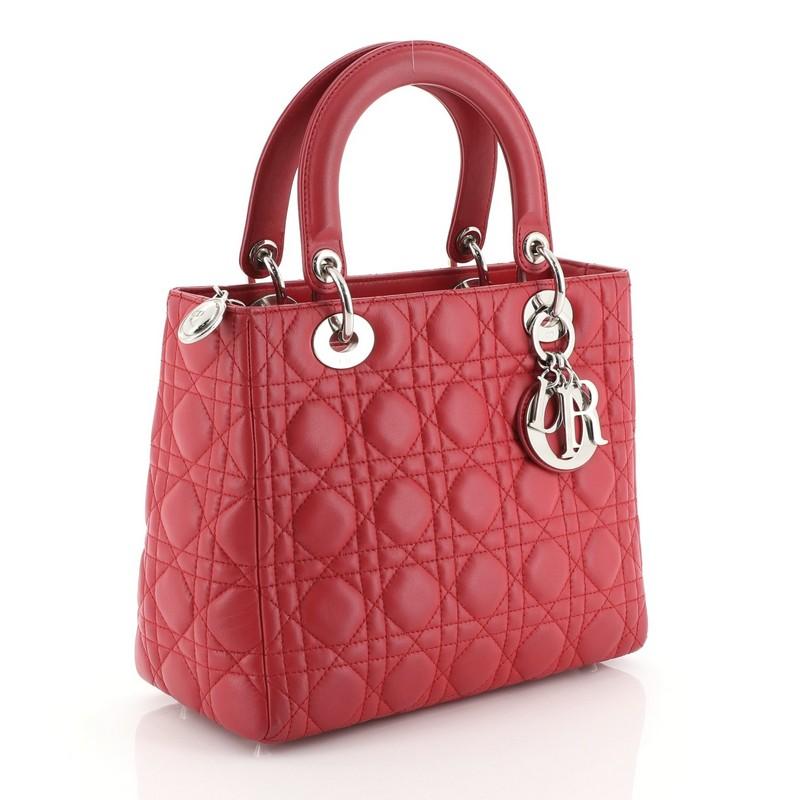 This Christian Dior Lady Dior Handbag Cannage Quilt Lambskin Medium, crafted in pink cannage quilted lambskin leather, features short dual handles with Dior charms and silver-tone hardware. Its top zip closure opens to a neutral fabric interior with