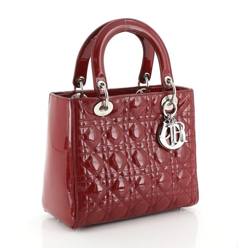 This Christian Dior Lady Dior Handbag Cannage Quilt Patent Medium, crafted in red cannage quilted patent leather, features dual top leather handles, Dior charms, and silver-tone hardware. Its zip closure opens to a red fabric interior with side zip